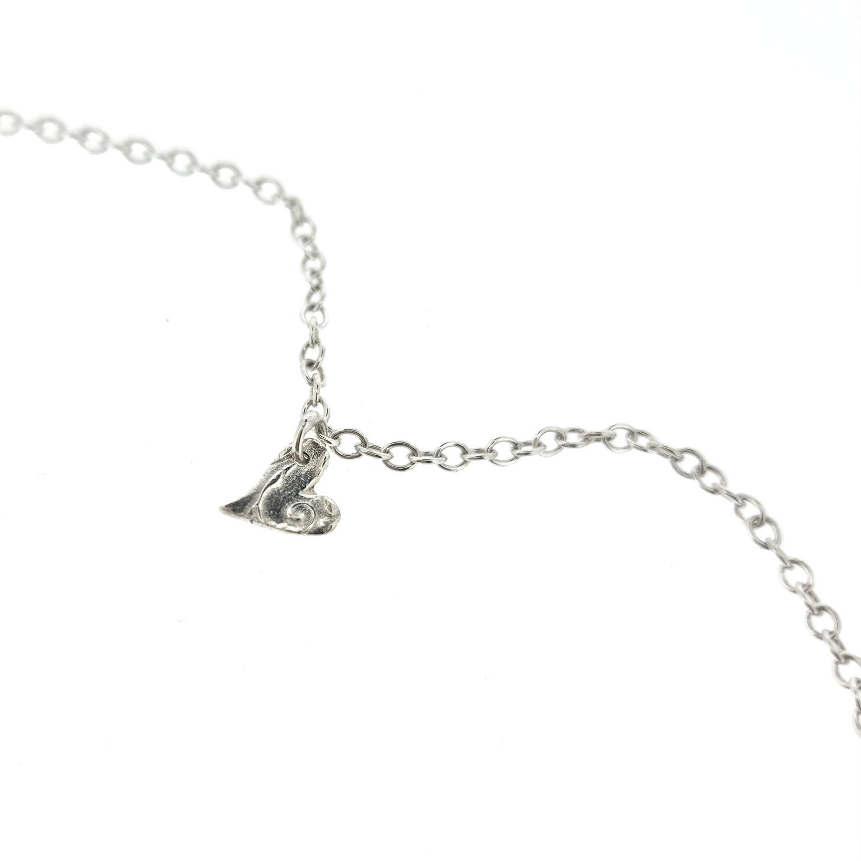 Sterling silver adjustable chain bracelet with small asymmetrical patterned heart charm.