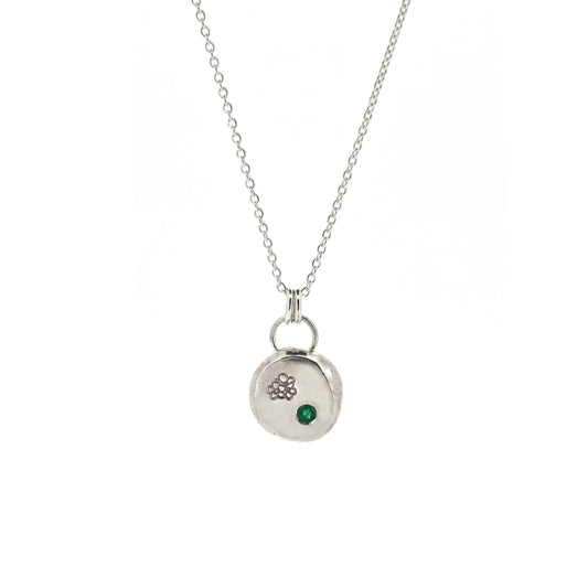 Round silver pendant necklace with a hawthorn flower engraved on it and a flush set green emerald gemstone. On a silver chain.
