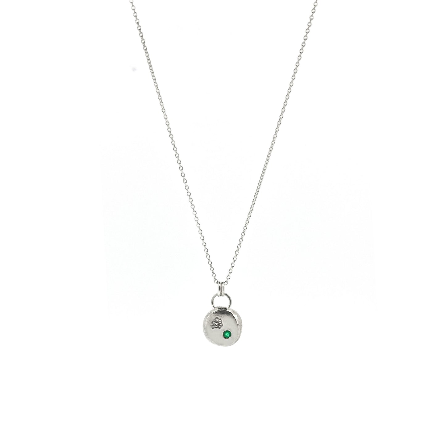 Round silver pendant necklace with a hawthorn flower engraved on it and a flush set green emerald gemstone. On a silver chain.