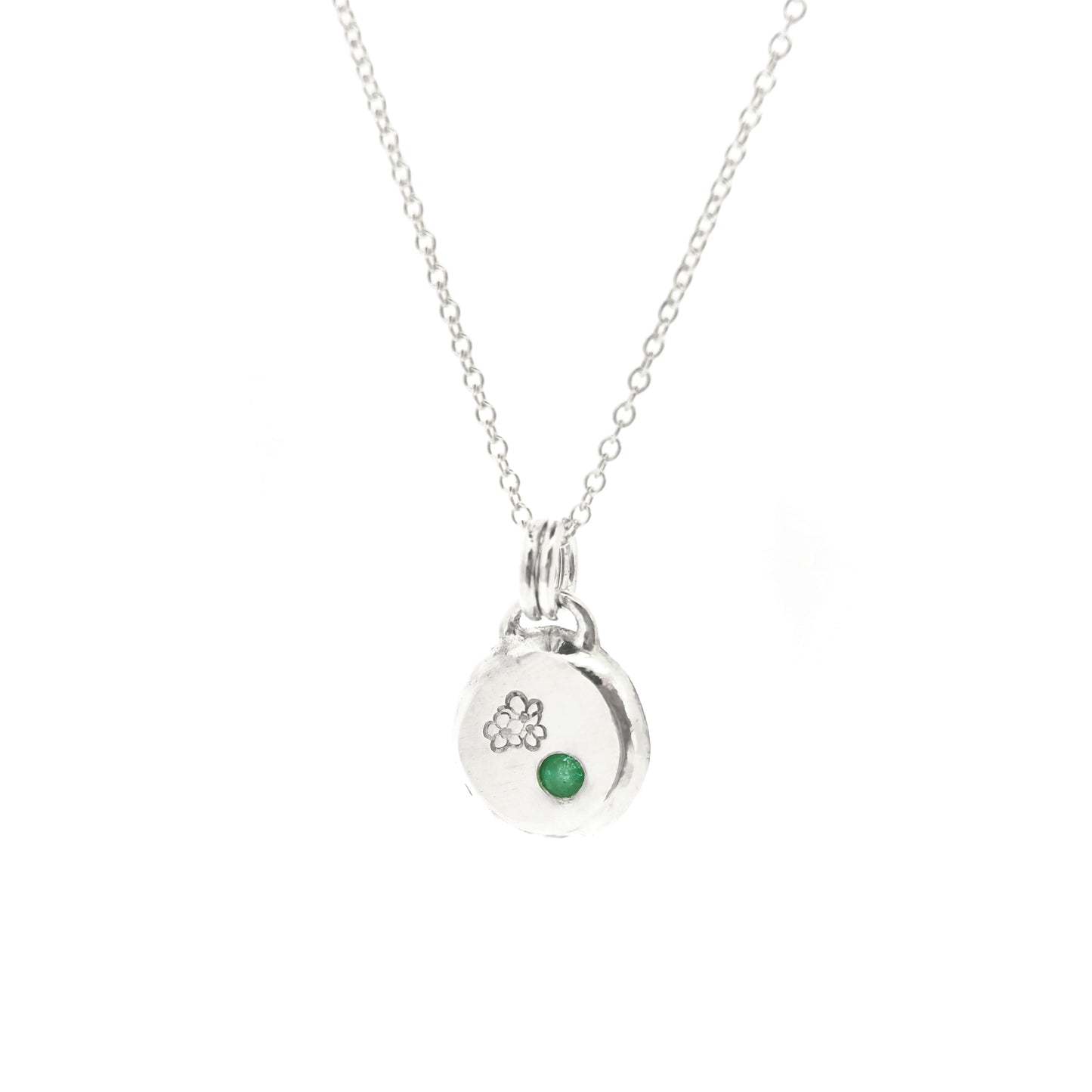 Round silver pendant necklace with a hawthorn flower engraved on it and a flush set green emerald gemstone. On a silver chain.