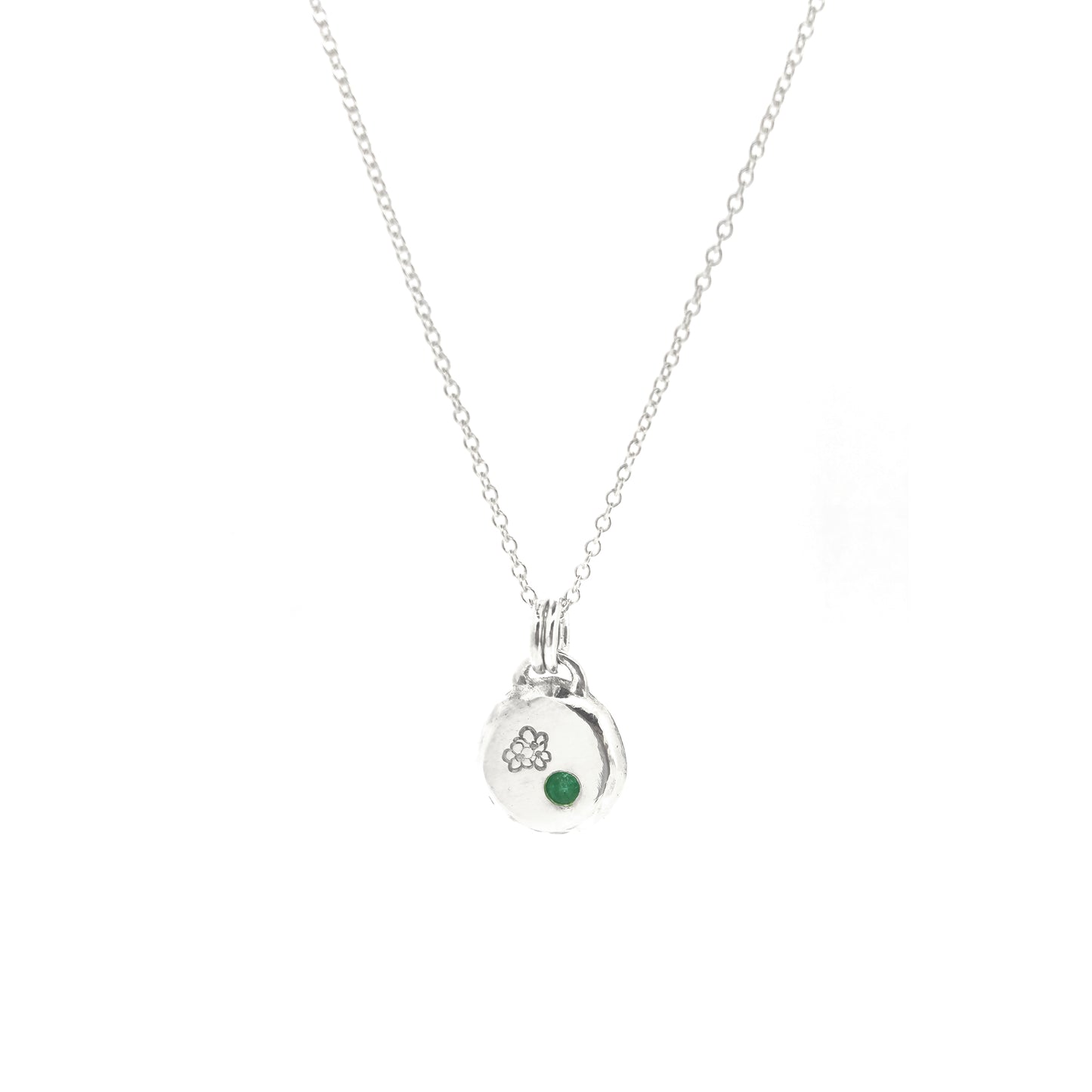 Round silver pendant necklace with a hawthorn flower engraved on it and a flush set green emerald gemstone. On a silver chain.