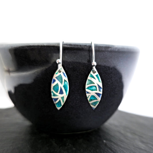 Silver drop earrings. Each earrings has a marquise shape with geometric cells containing blue, green and turquoise enamel. Pictured on a black bowl.