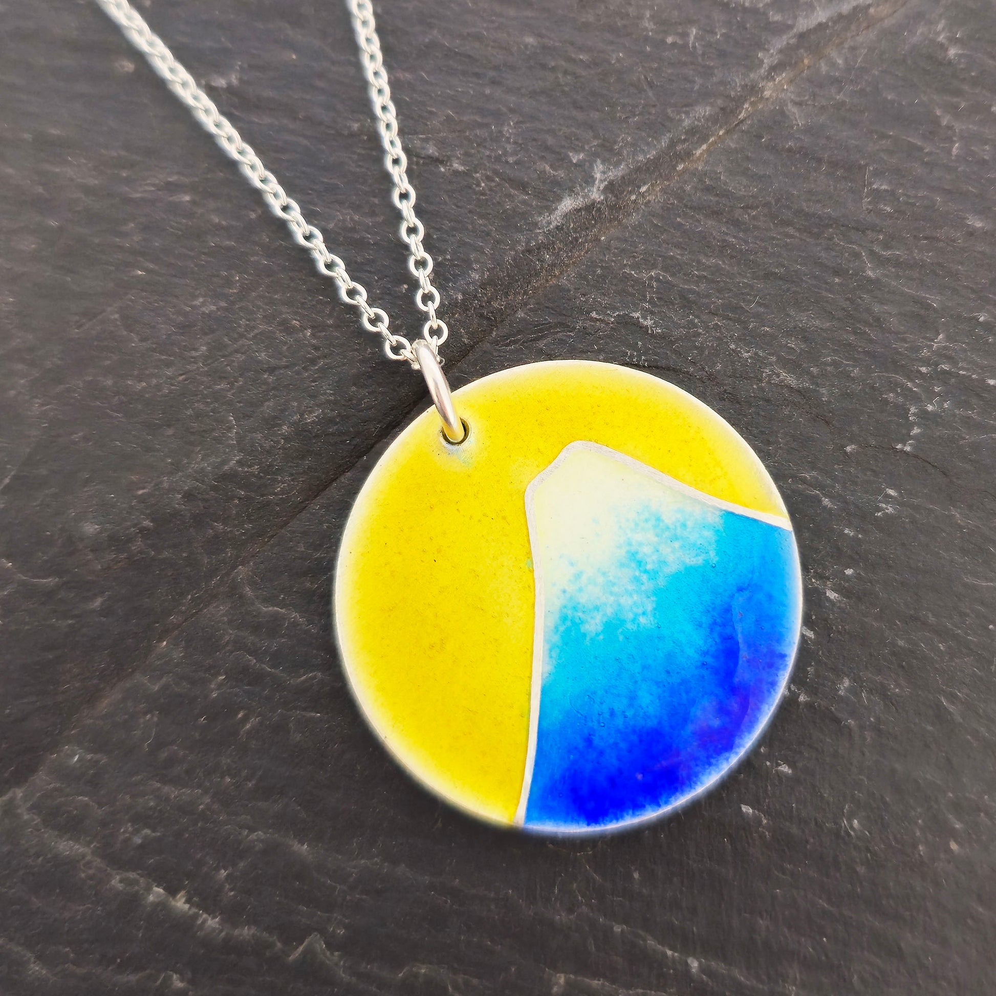 Round silver pendant with a mountain on in graduated blue enamel and a white top and a yellow enamel background. Suspended from a silver chain. Handmade. Mijoux Jewellery.