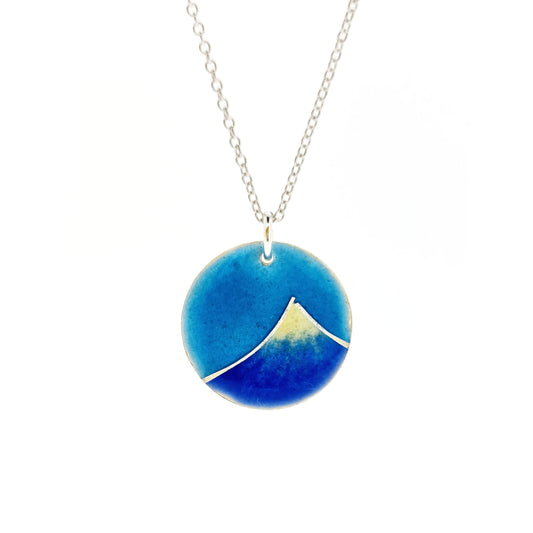 Silver and enamel round pendant featuring a dark blue and white mountain with a turquoise blue sky. On a silver chain.