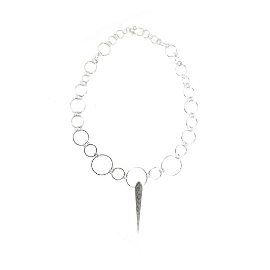 Silver elongated patterned teardrop pendant on a handmade circle link chain with circles of differing sizes.