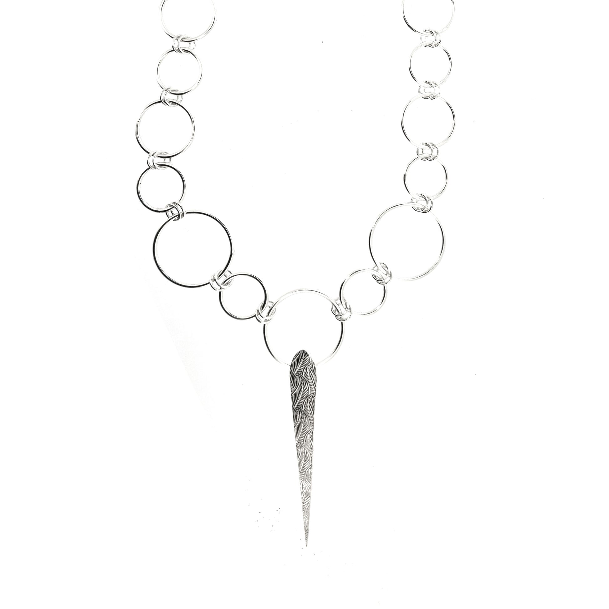 Silver elongated patterned teardrop pendant on a handmade circle link chain with circles of differing sizes.