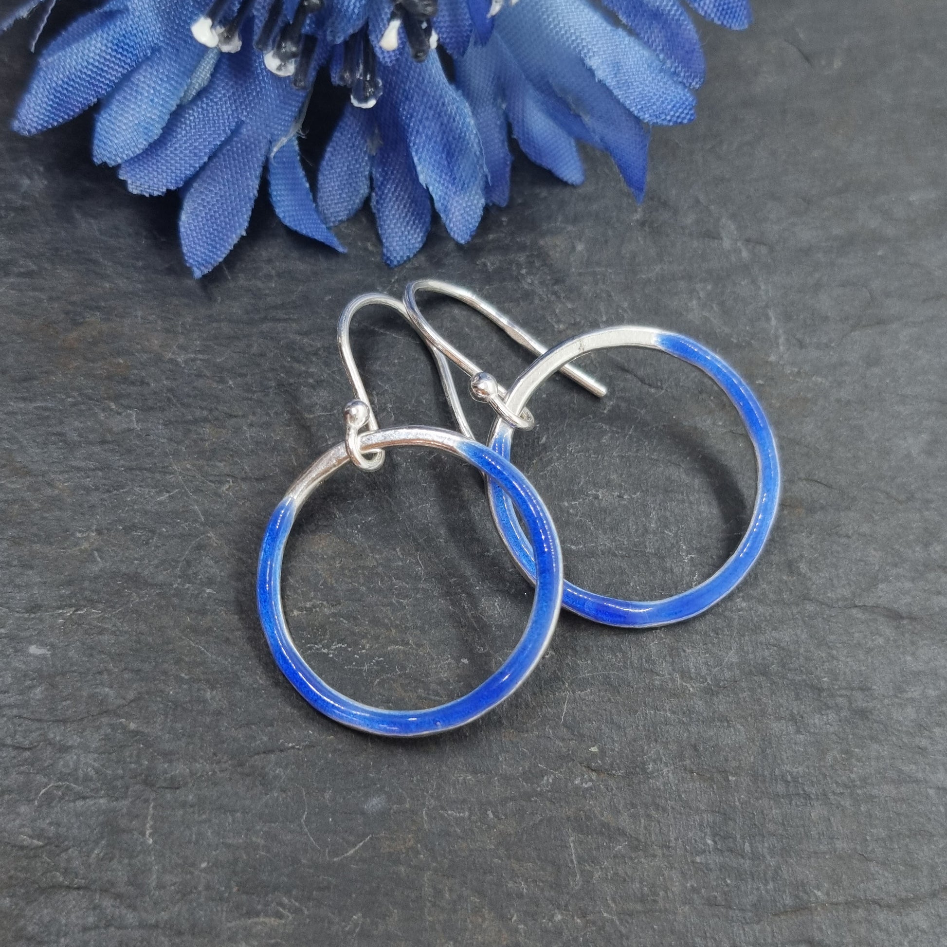 Silver open circle drop earrings with royal blue enamel. Shown with blue flower.