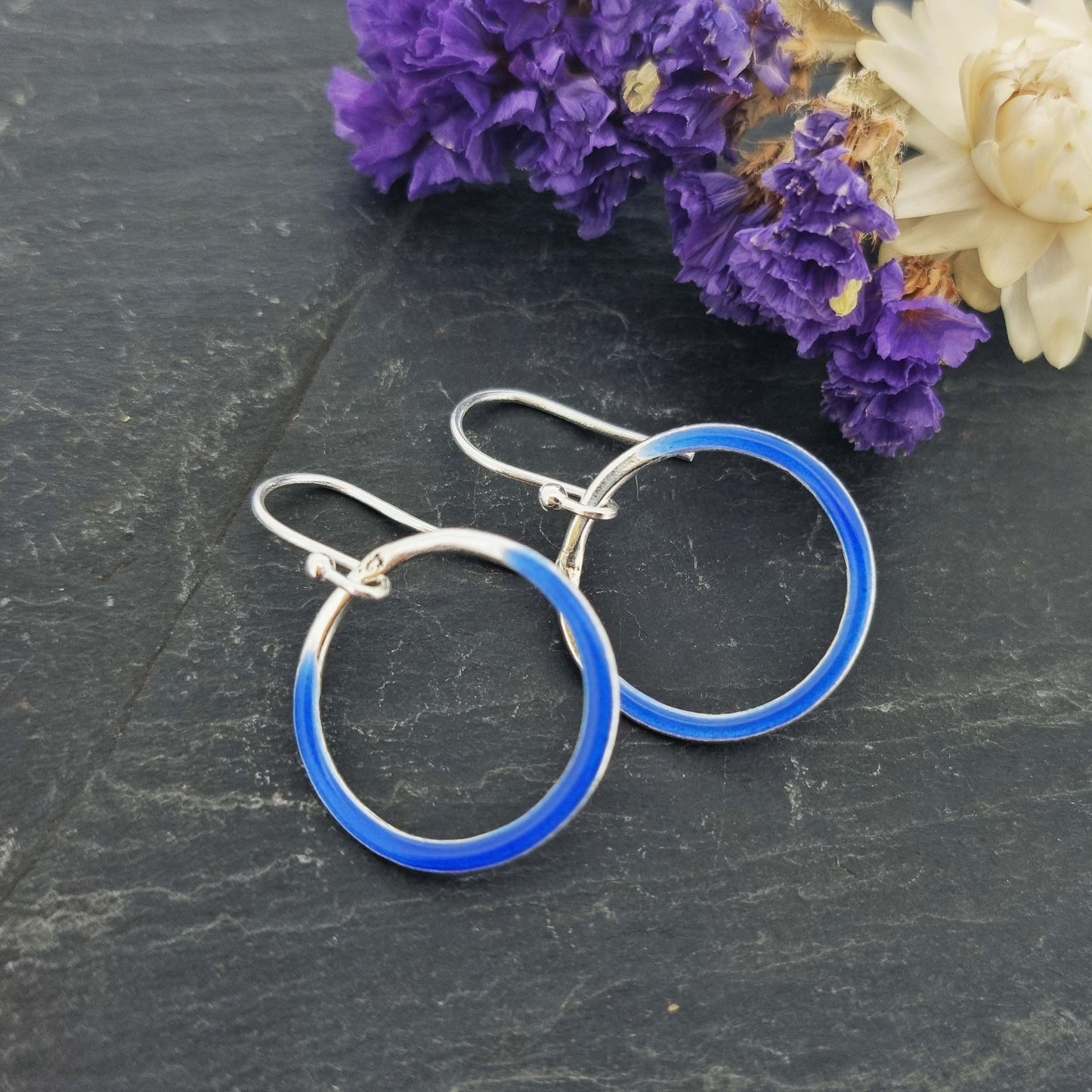 Silver open circle drop earrings with royal blue enamel. Shown with flowers.