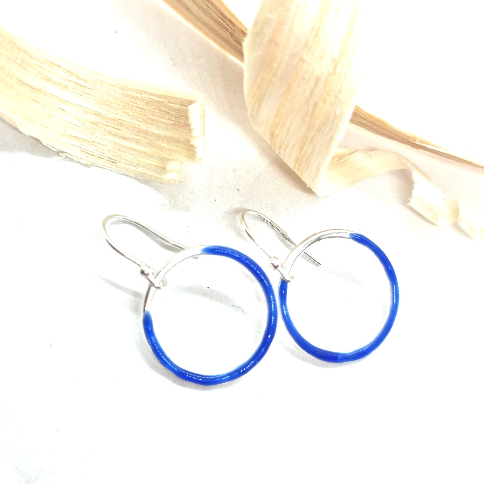 Silver open circle drop earrings with royal blue enamel. Shown with wood shavings.