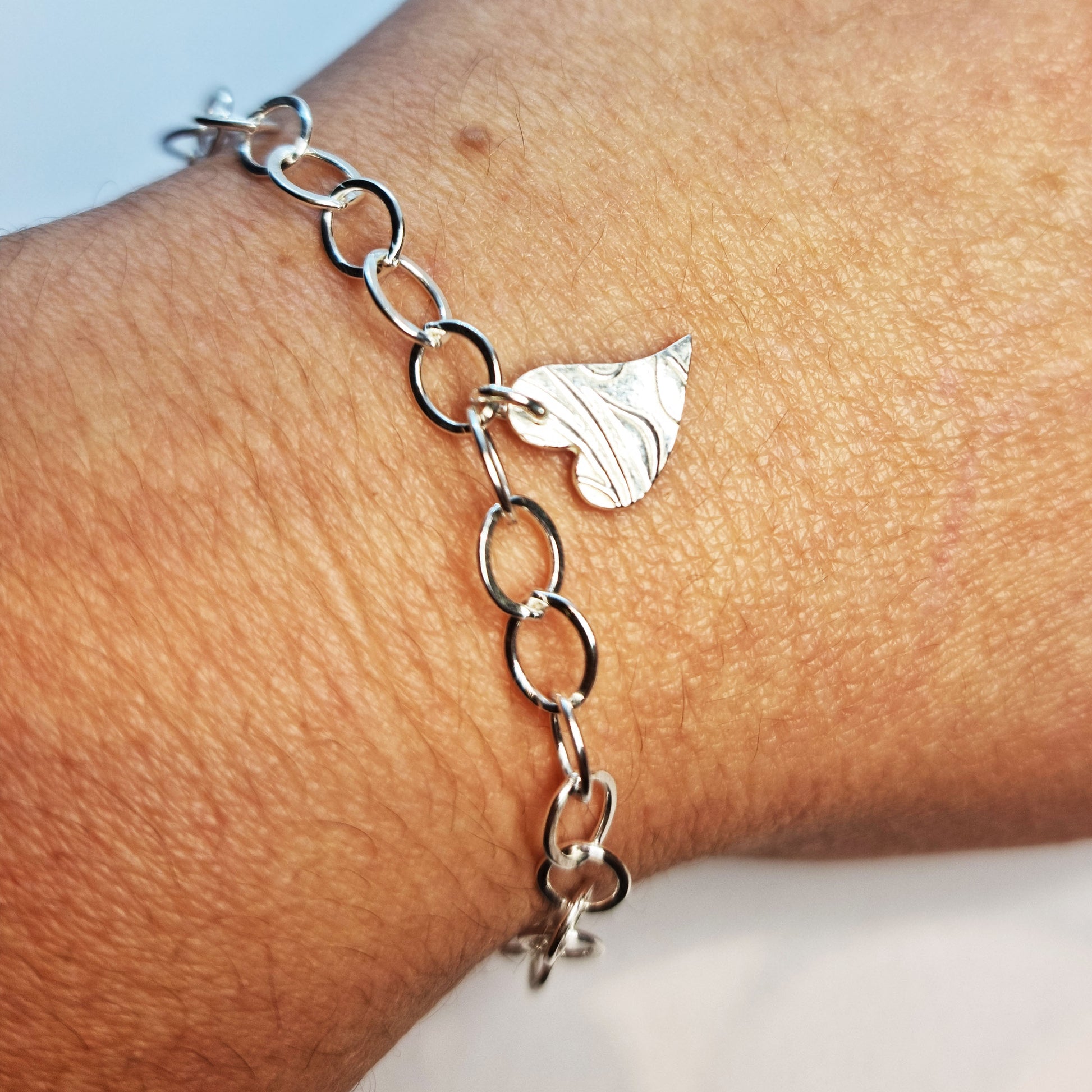Silver large link chain bracelet with asymmetrical patterned heart charm. Shown on wrist
