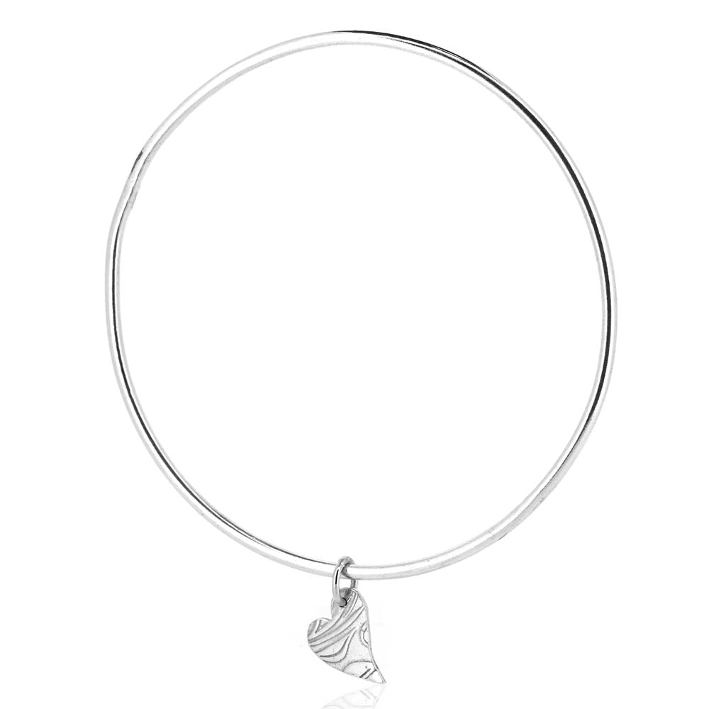 A round silver bangle with an asymmetrical patterned heart charm.