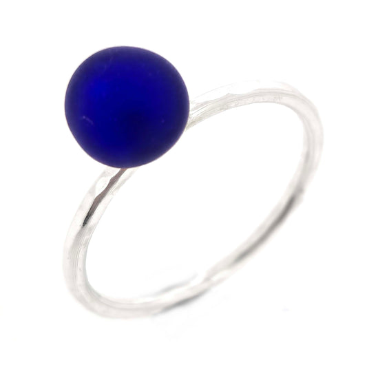 A silver stacking ring with a thin silver band with a hammered finish and a dark blue glass sphere on top. Mijoux Creations.