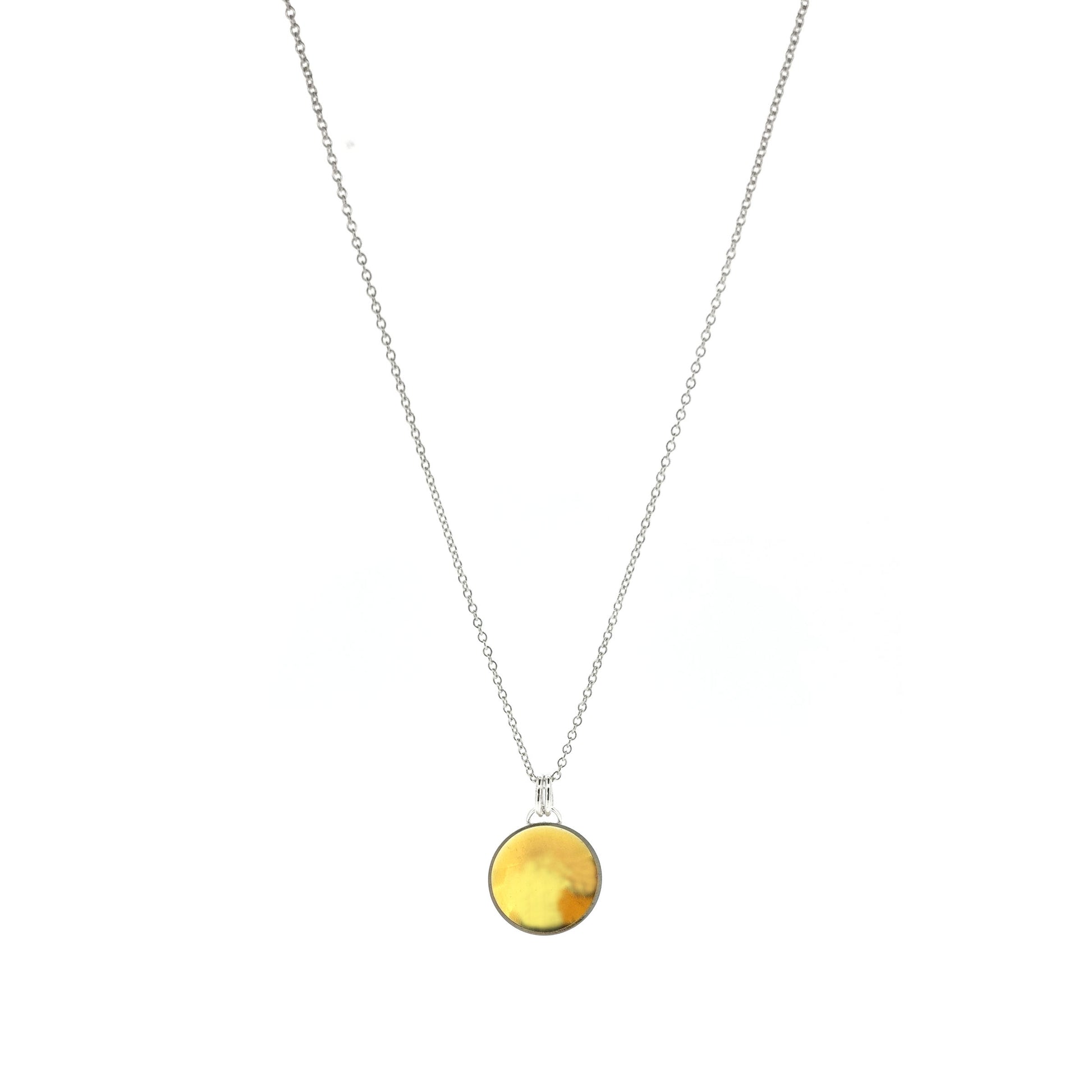 A silver round domed pendant with a gold center and double bail suspended from a silver chain.