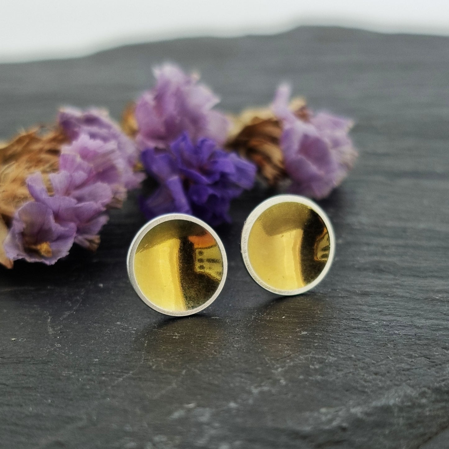 Silver round stud earrings with a gold center. Pictured with flowers.