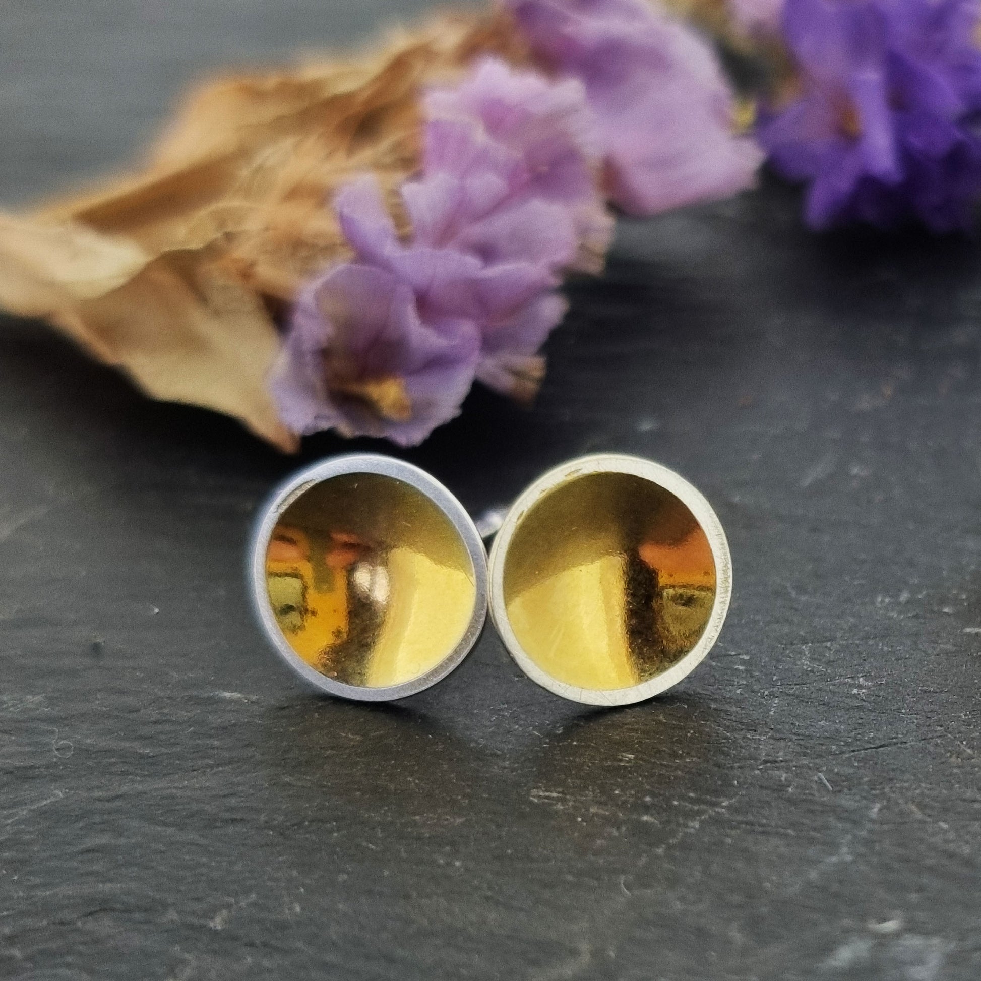 Silver round stud earrings with a gold center. Pictured with flowers.