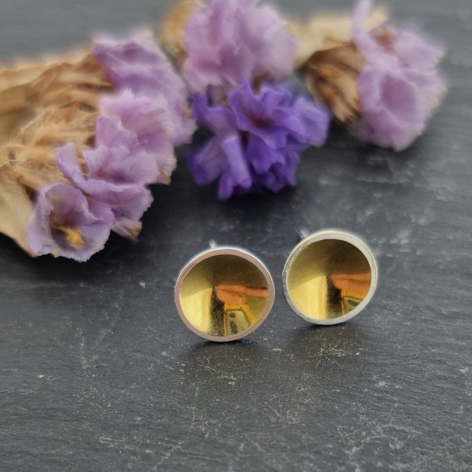 Silver round stud earrings with a gold center. Pictured with flowers.