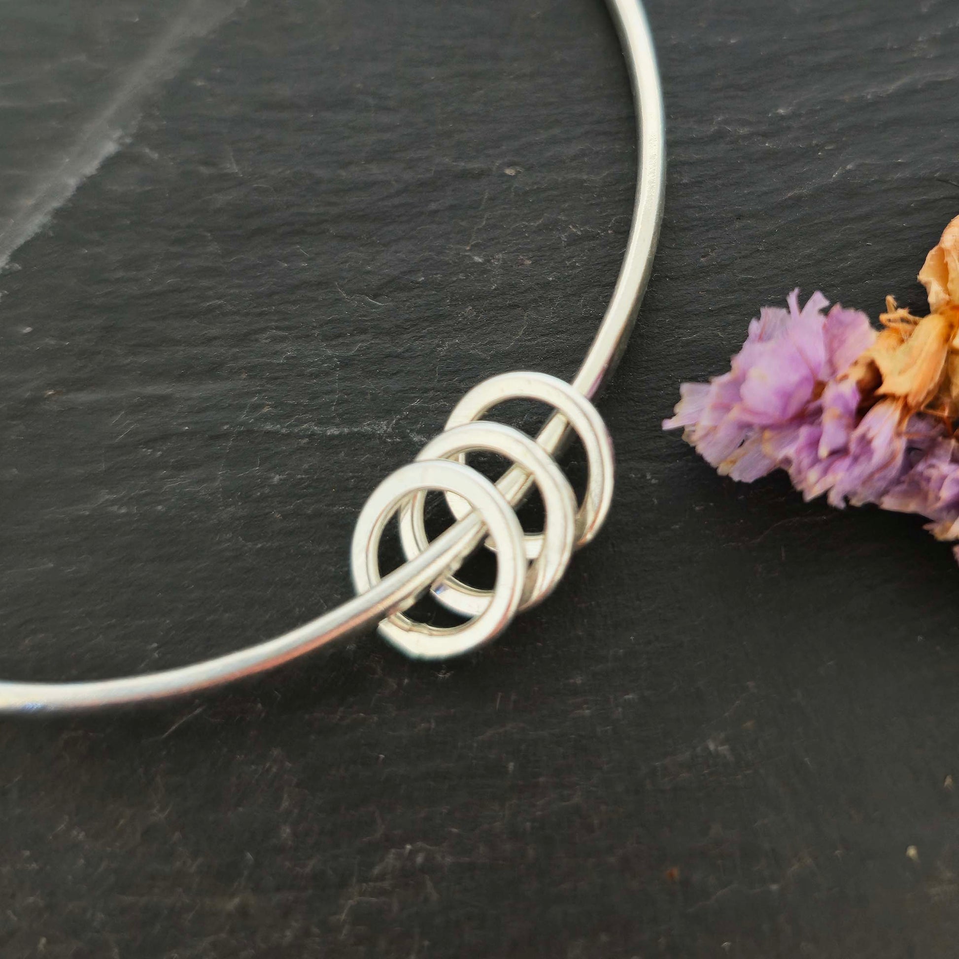 Section of a silver textured bangle with 3 circle beads on a dark slate background with flowers