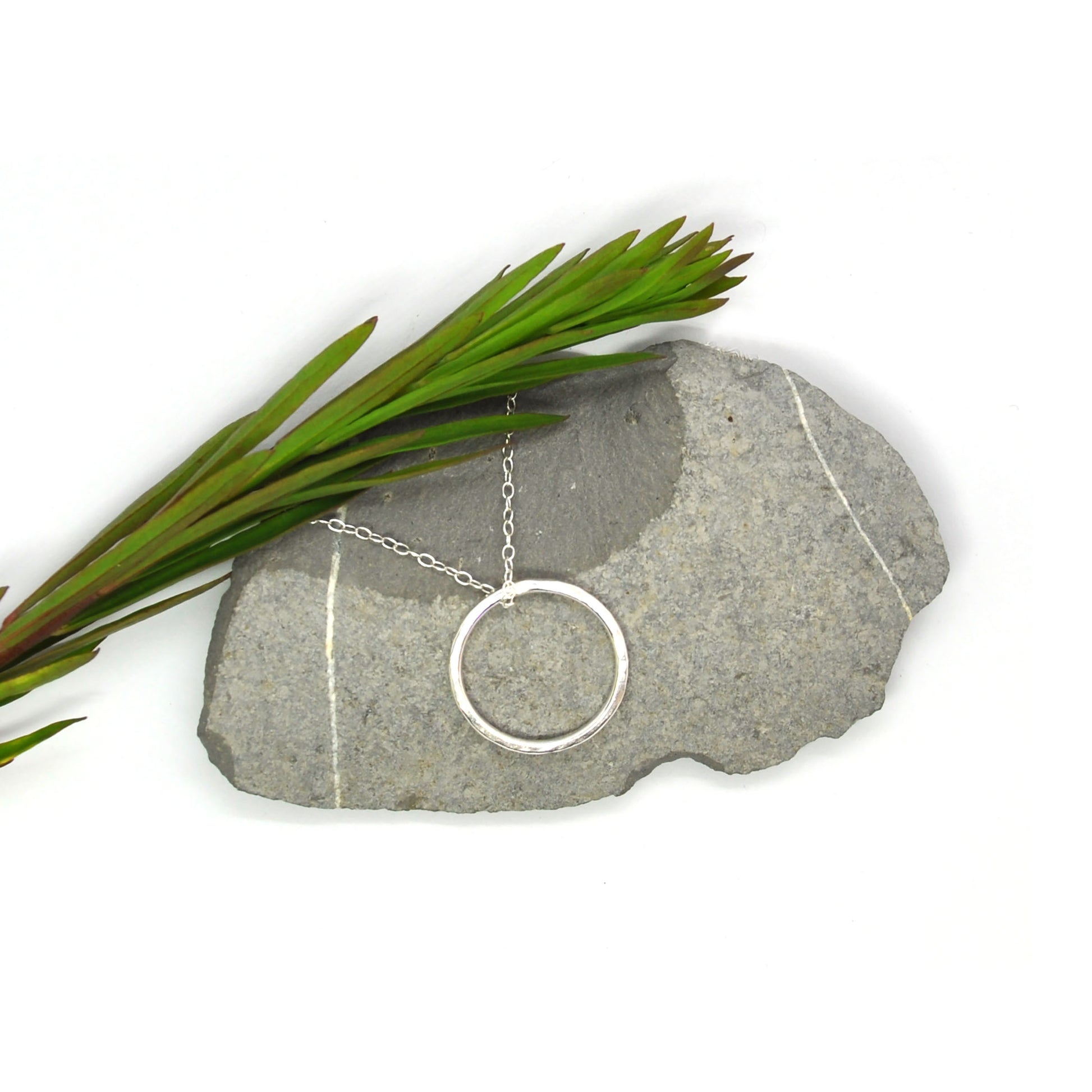 Silver hammered open circle pendant on silver chain - large on pebble with greenery