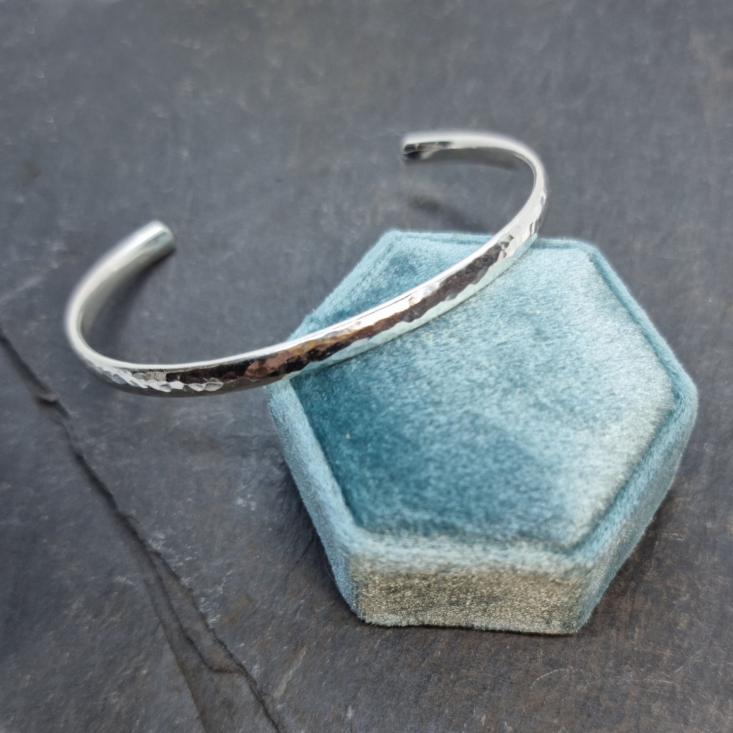 Silver hammered open torque bangle. Pictured resting on a box.