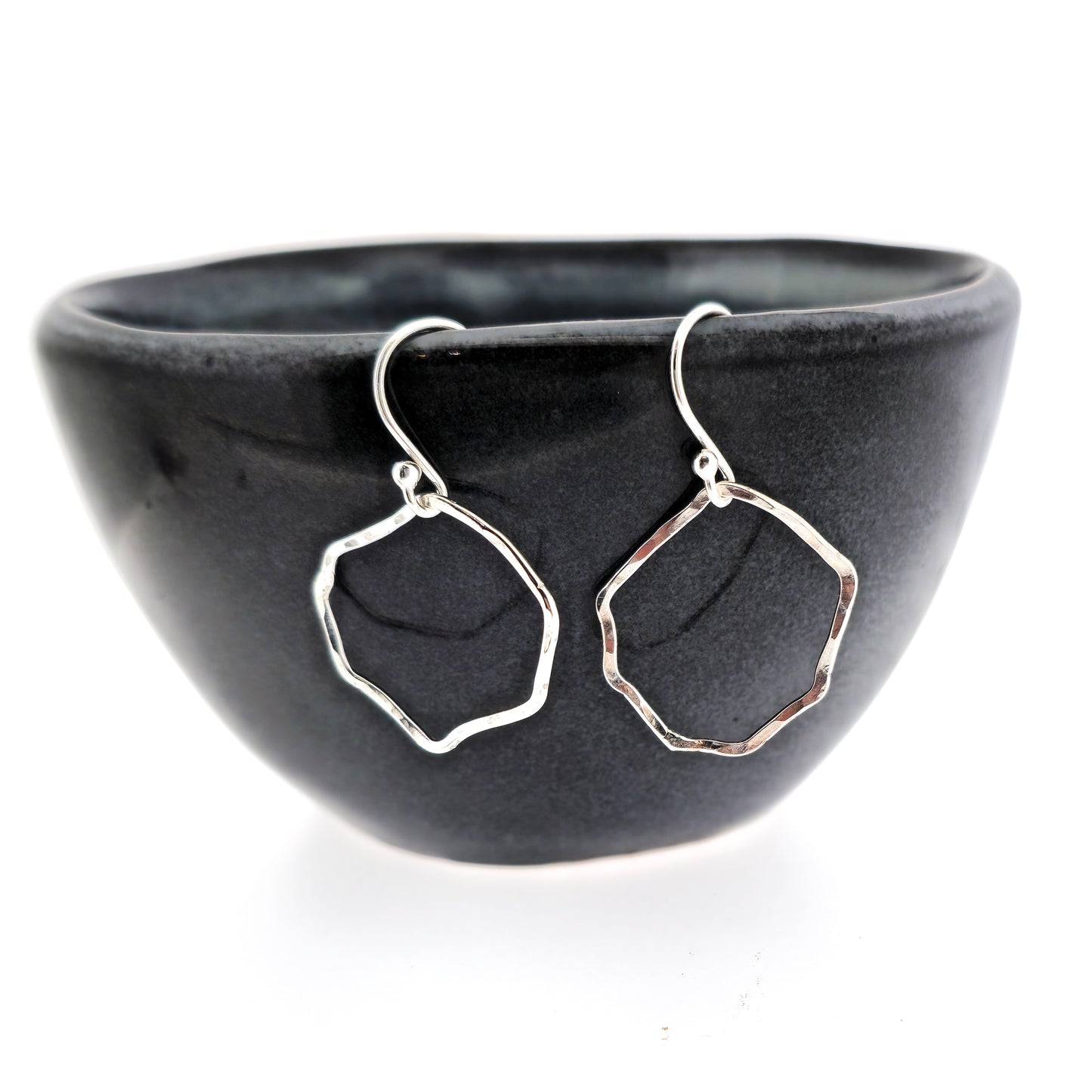 Silver drop earrings with an open organic rustic style circle suspended from silver ear wires - large. Shown on a black bowl.