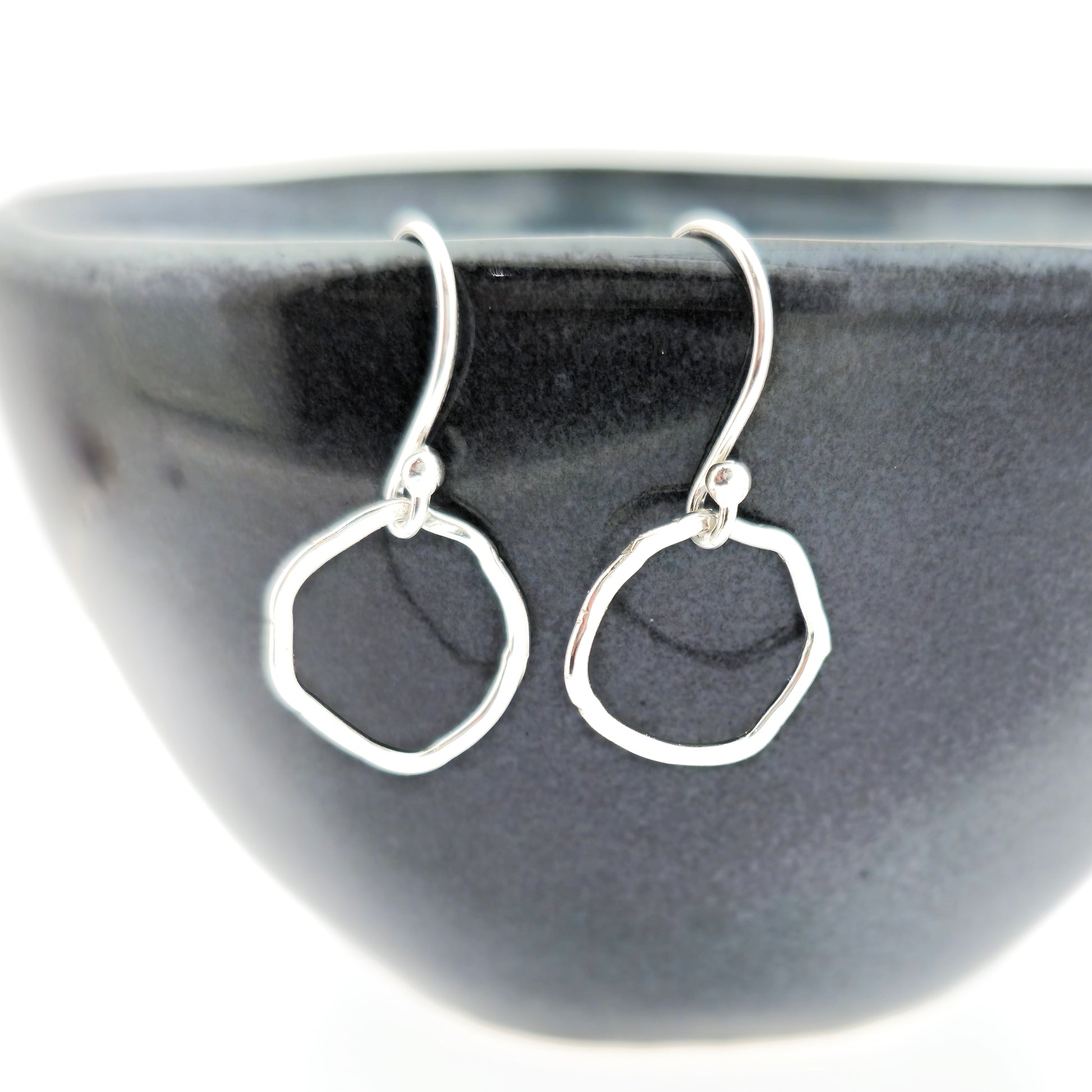 Silver drop earrings with an open organic rustic style circle suspended from silver ear wires - small. Shown on a black bowl.