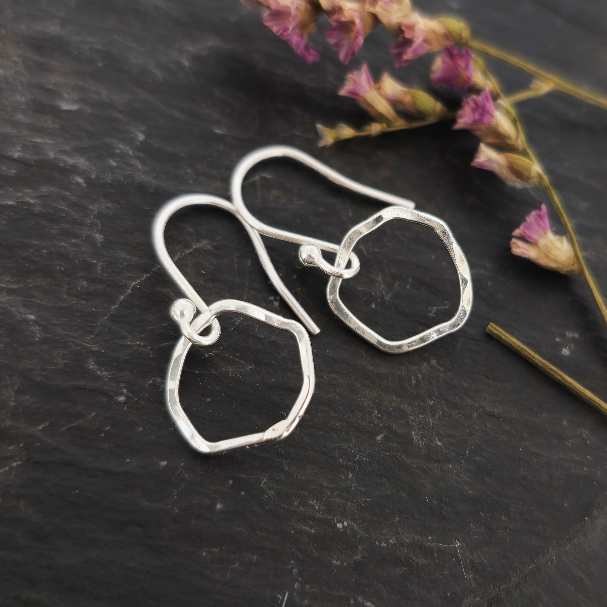 Silver drop earrings with an open organic rustic style circle suspended from silver ear wires - small. Shown on slate with flowers.