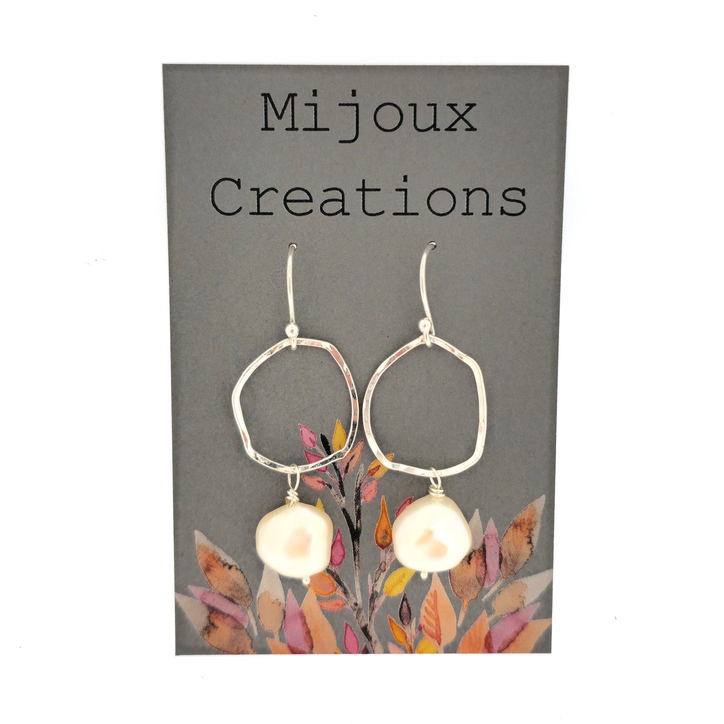 Silver drop earrings consisting of an organic rustic style open circle with a hammered finish suspended from silver ear hooks and with a white pearl hanging from it. Large. Pictured on a Mijoux card.