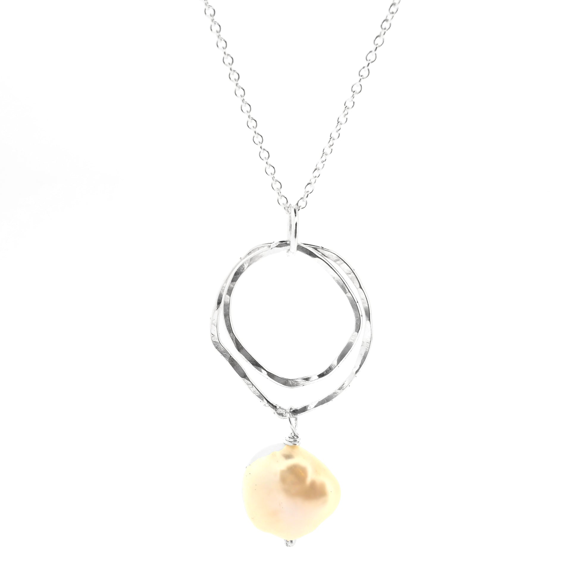 A silver pendant consisting of two organic rustic style open circles of different sizes with a hammered finish and an ivory pearl suspended beneath. Hanging from a silver chain.