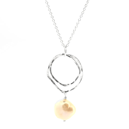 A silver pendant consisting of two organic rustic style open circles of different sizes with a hammered finish and an ivory pearl suspended beneath. Hanging from a silver chain.