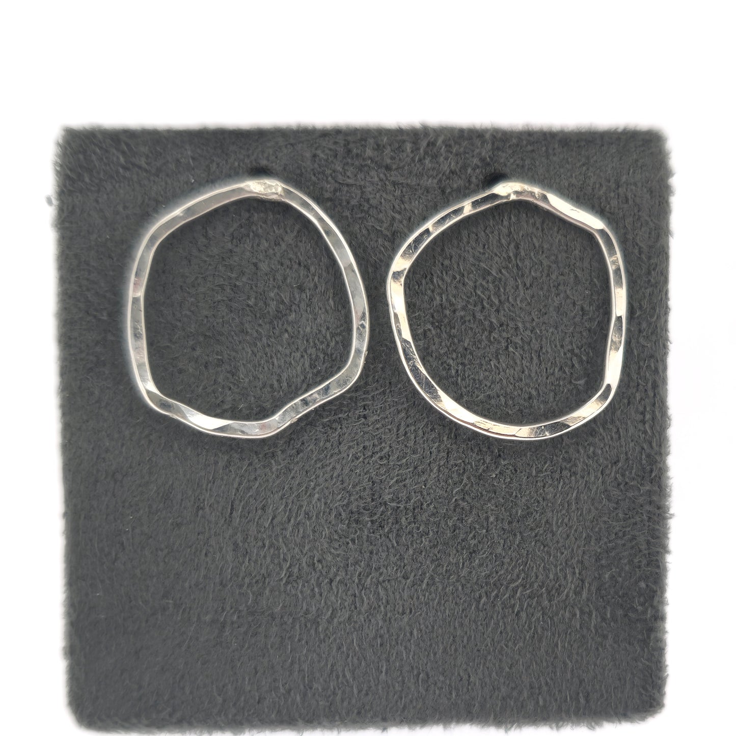 Silver open stud earrings of an organic rustic circle shape - large. Shown on a grey stand.