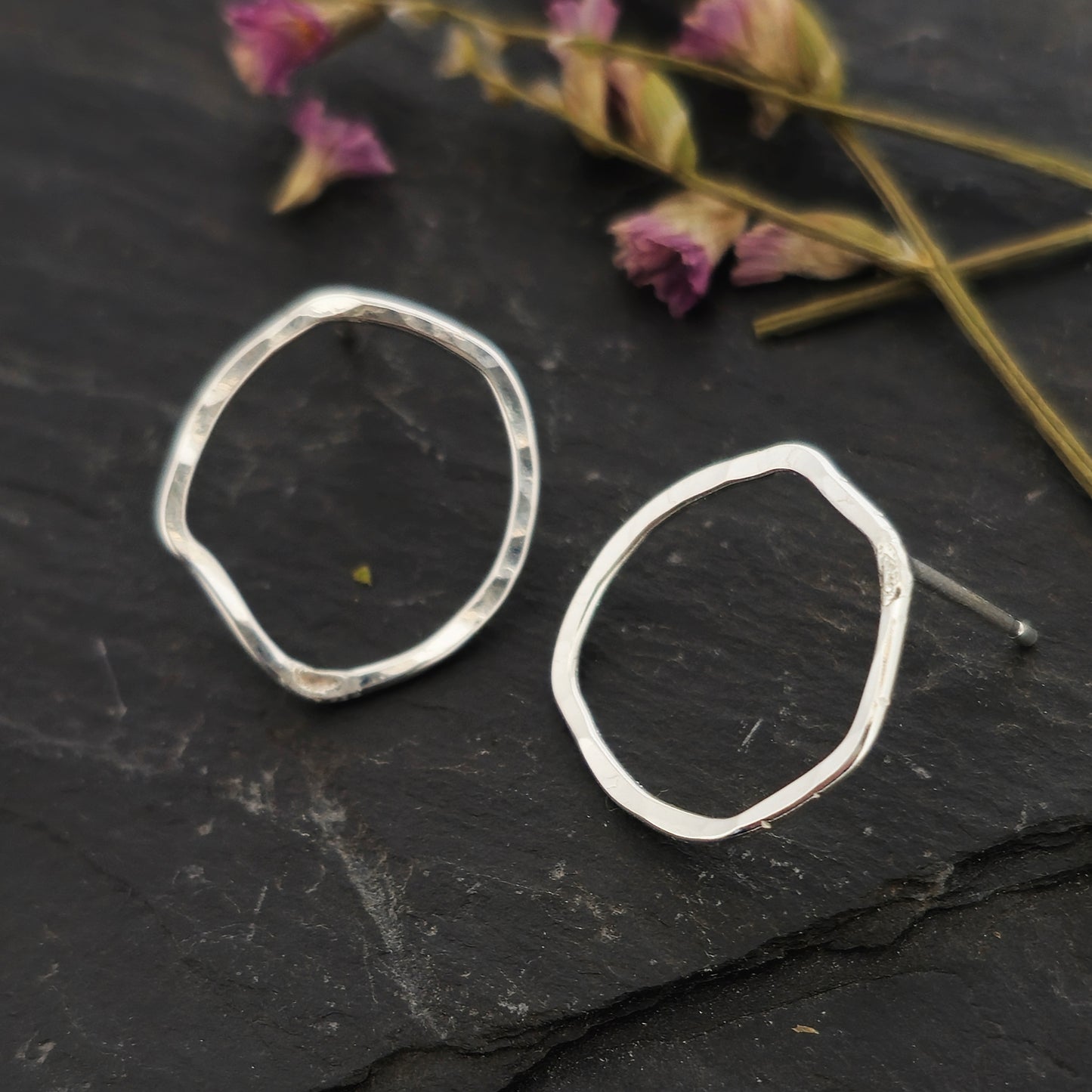 Silver open stud earrings of an organic rustic circle shape - large. Shown on slate with flowers.