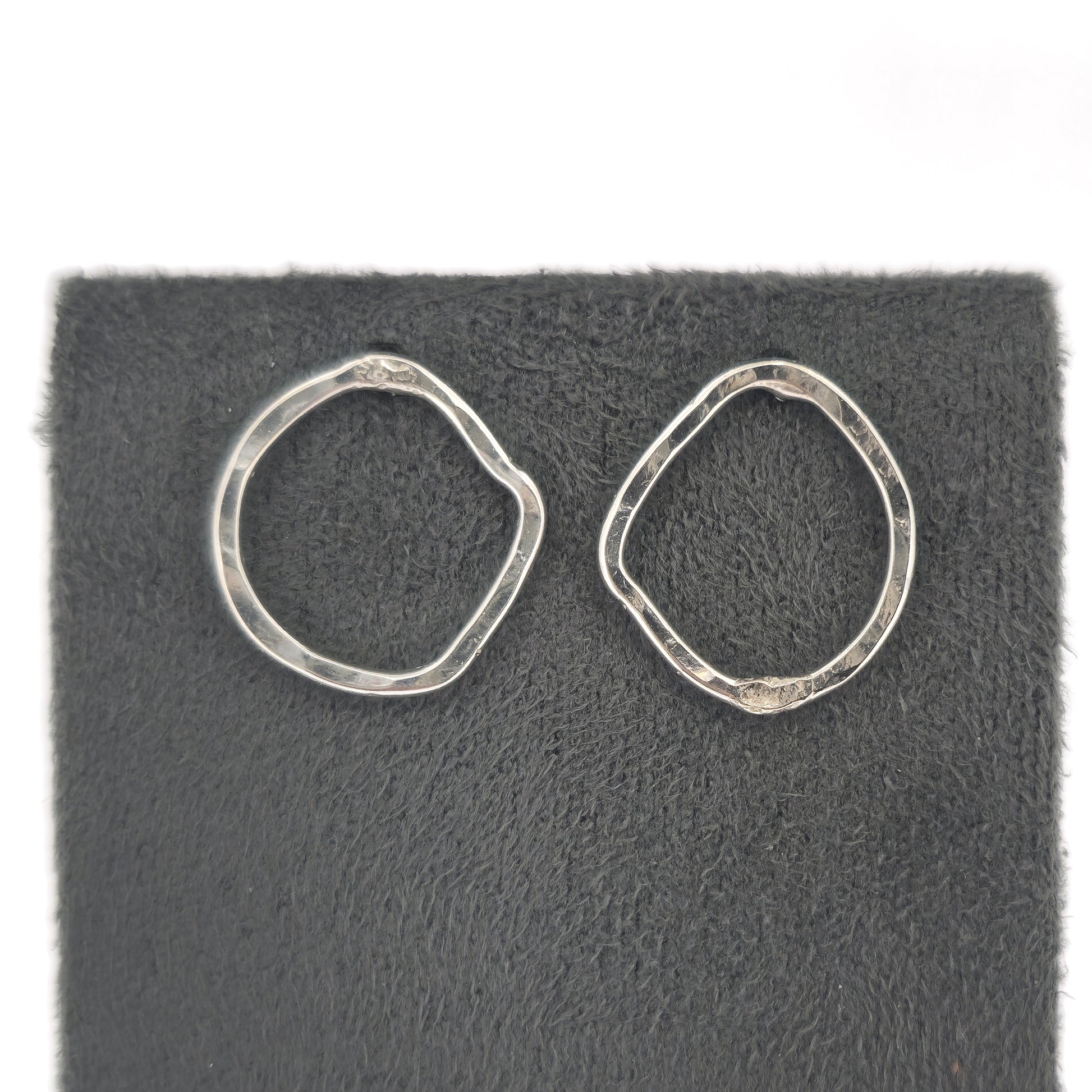 Silver open stud earrings of an organic rustic circle shape - small. Shown on a grey stand.