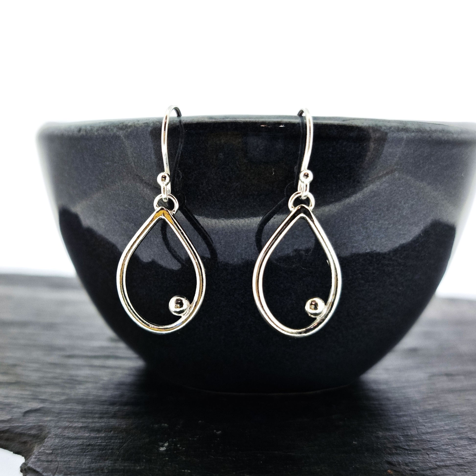 Silver drop earrings featuring an open teardrop shape with an off-centre ball. Medium.