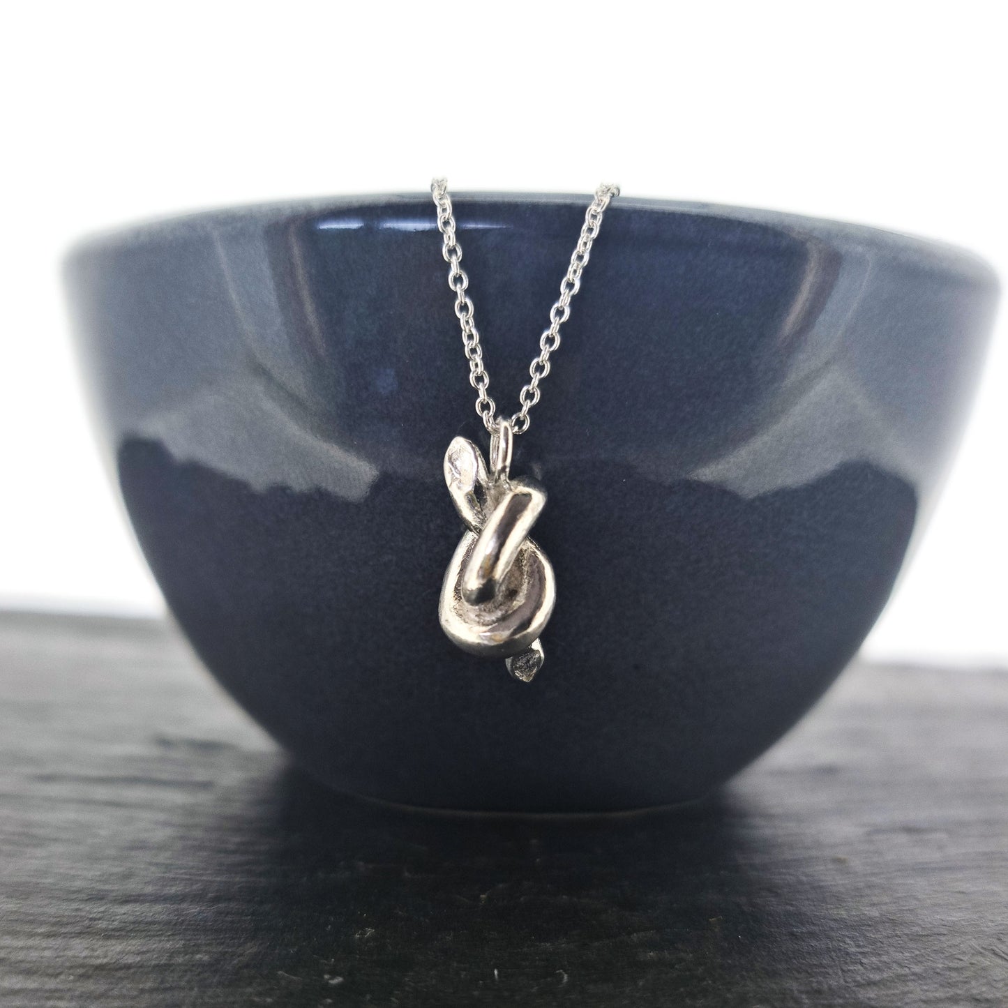 Silver chain with a silver knot pendant. Shown on a black bowl.