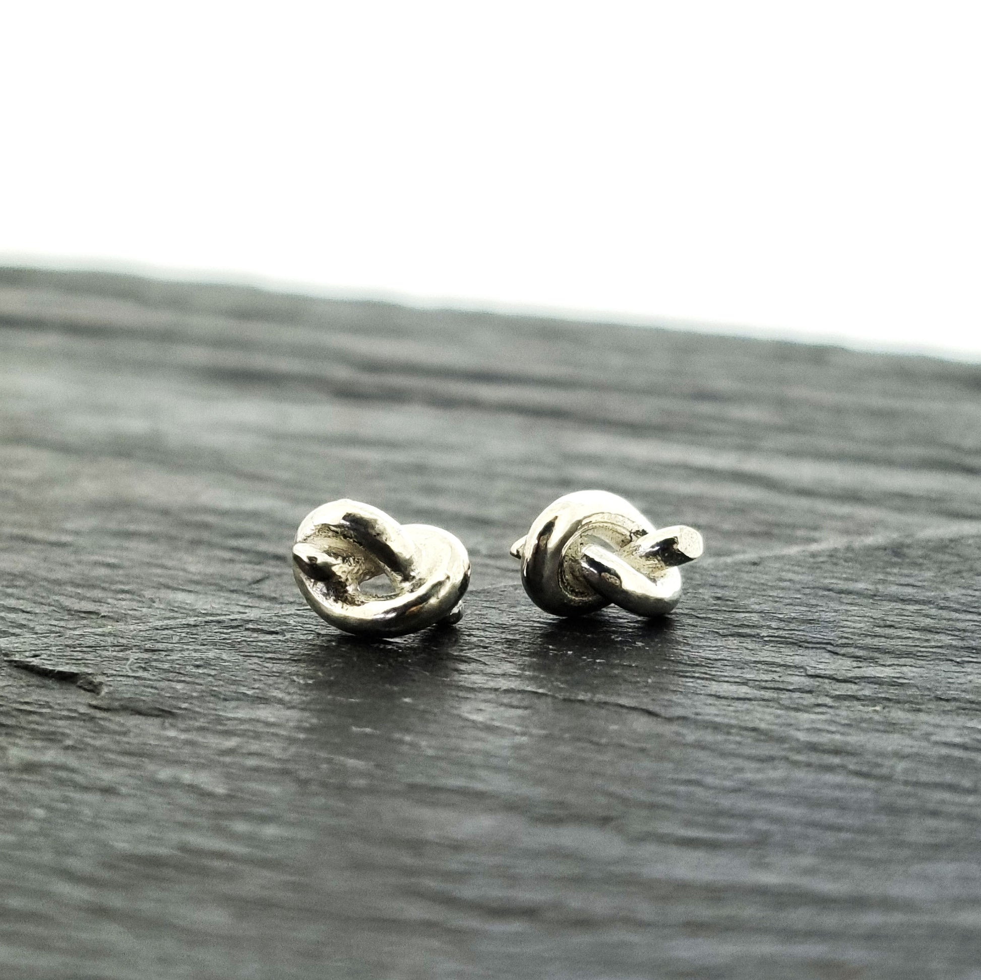 Silver stud earrings in the shape of a knot in a piece of string.