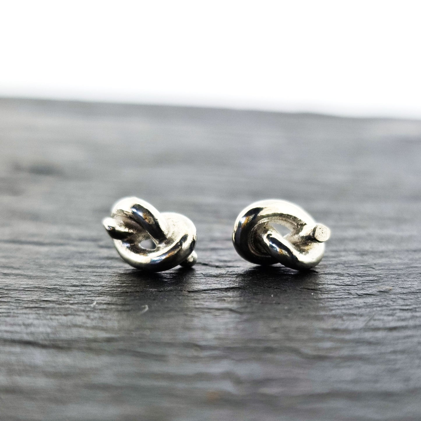 Silver stud earrings in the shape of a knot in a piece of string.