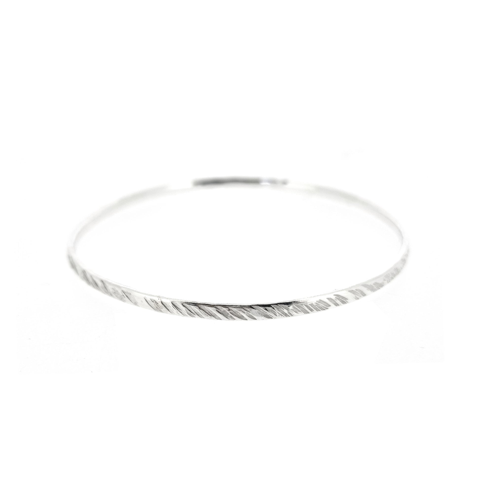 A silver round bangle with a diagonal rustic lined texture.