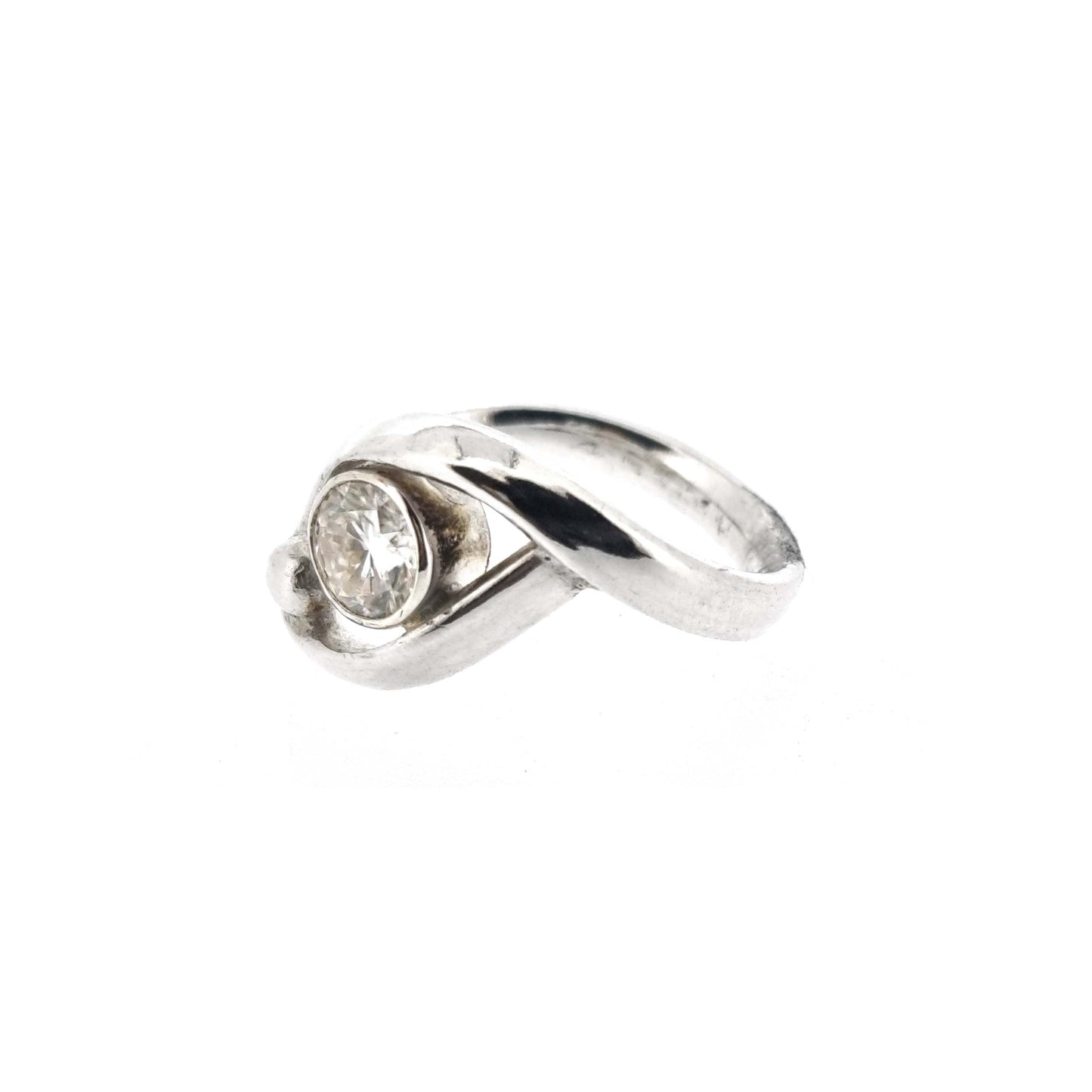 A silver ring with a central round faceted moissanite gemstone in a bezel setting. Next to the gemstone is a silver ball and the band of the ring wraps around both the ball and gemstone.