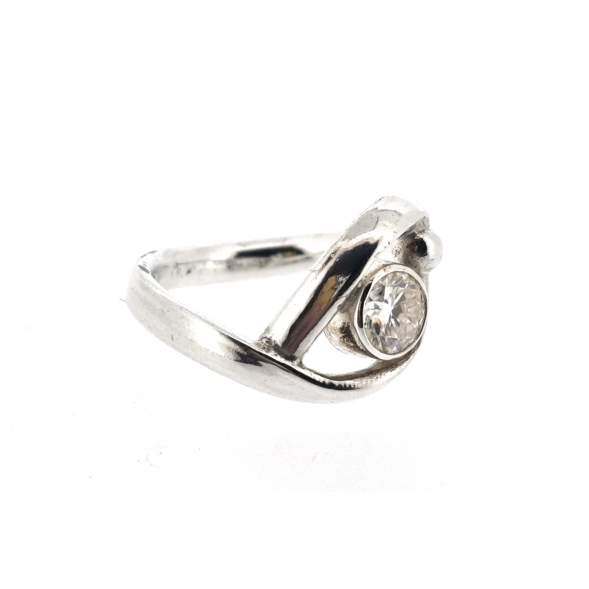 A silver ring with a central round faceted moissanite gemstone in a bezel setting. Next to the gemstone is a silver ball and the band of the ring wraps around both the ball and gemstone.