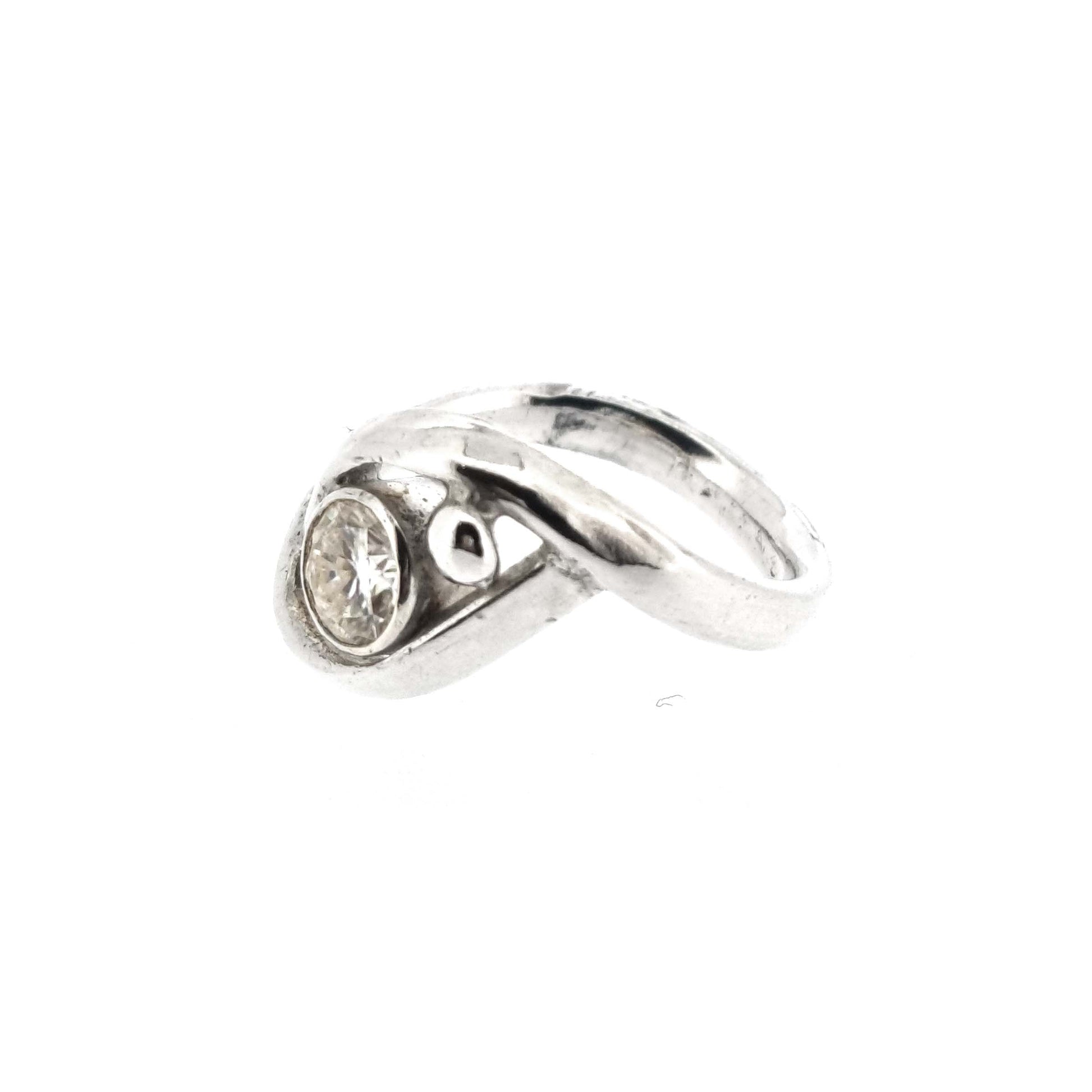 A silver ring with a central round faceted moissanite gemstone in a bezel setting. Next to the gemstone is a silver ball and the band of the ring wraps around both the ball and gemstone.