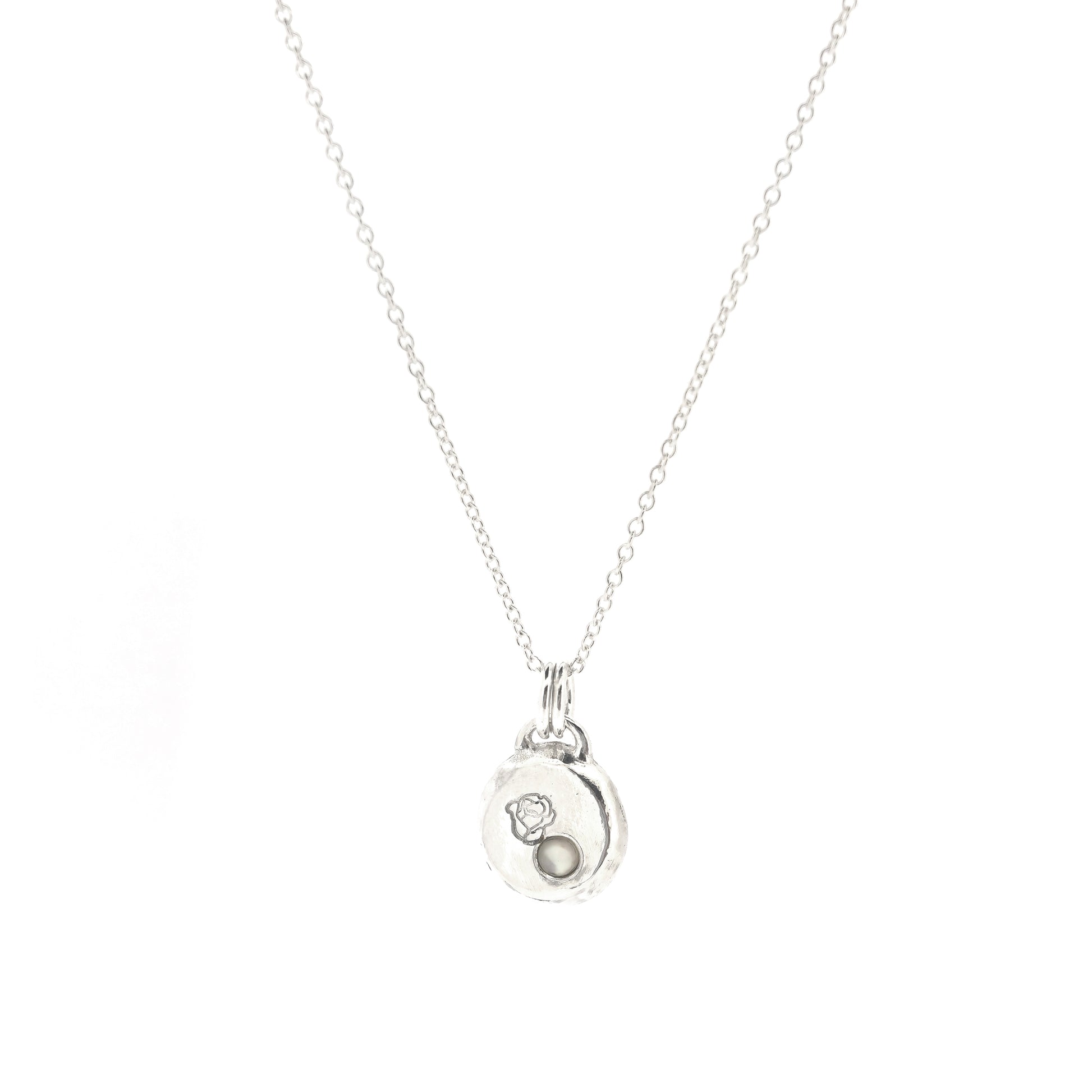 A round silver flat pebble pendant necklace with a rose engraved on it and a flush-set mother of pearl gemstone.