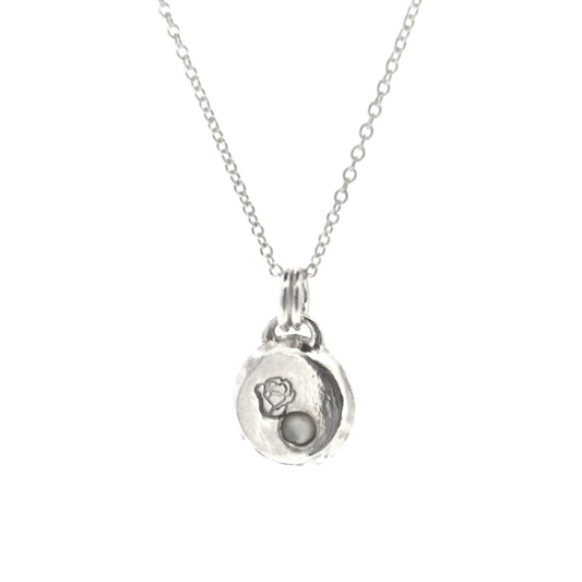 A round silver flat pebble pendant necklace with a rose engraved on it and a flush-set mother of pearl gemstone.