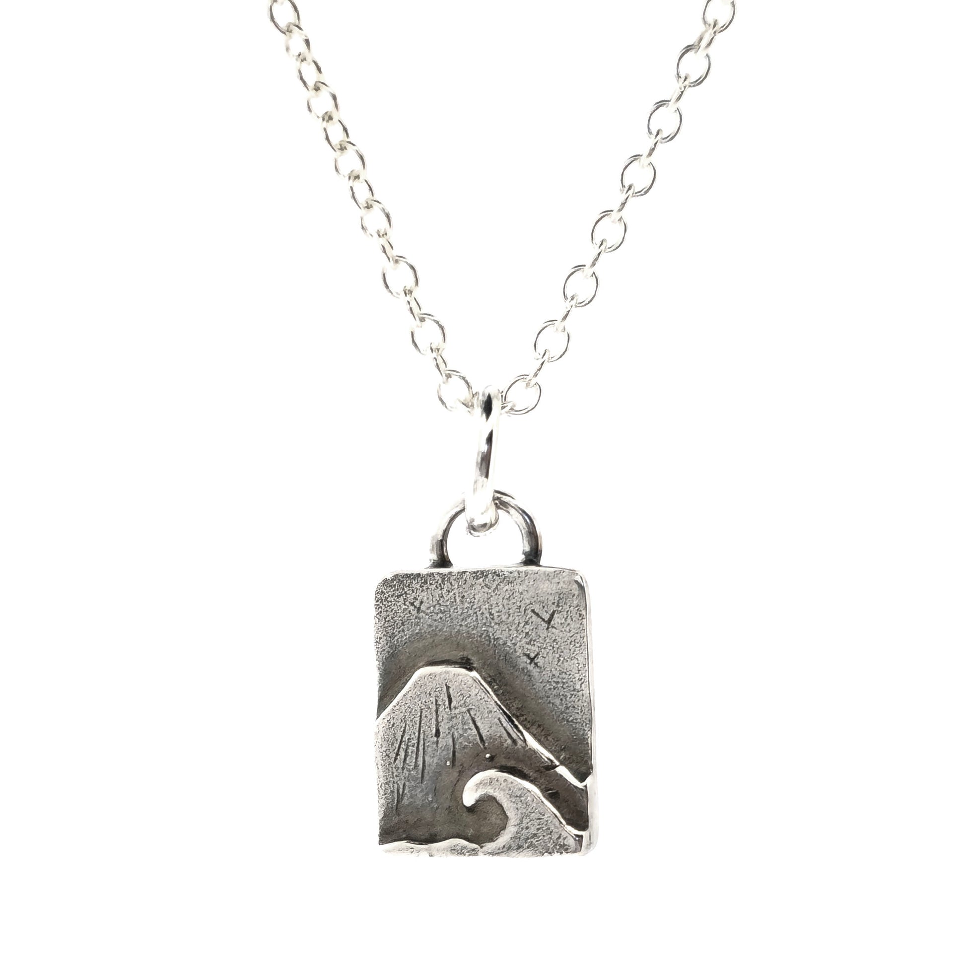 A rectangular silver handmade pendant featuring a mountain with a sea and wave in front and birds flying in the sky. Suspended from a silver chain. On a white background. Mijoux jewellery.