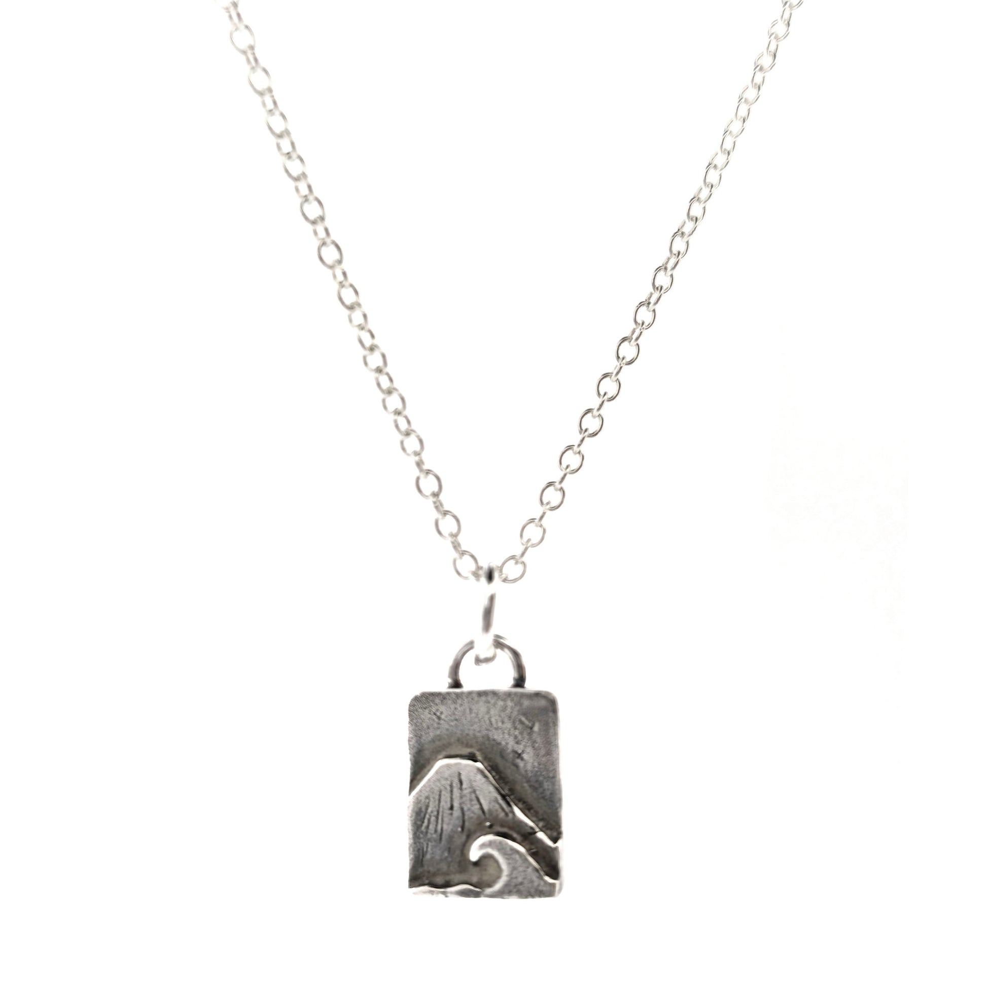 A rectangular silver handmade pendant featuring a mountain with a sea and wave in front and birds flying in the sky. Suspended from a silver chain. On a white background. Mijoux jewellery.