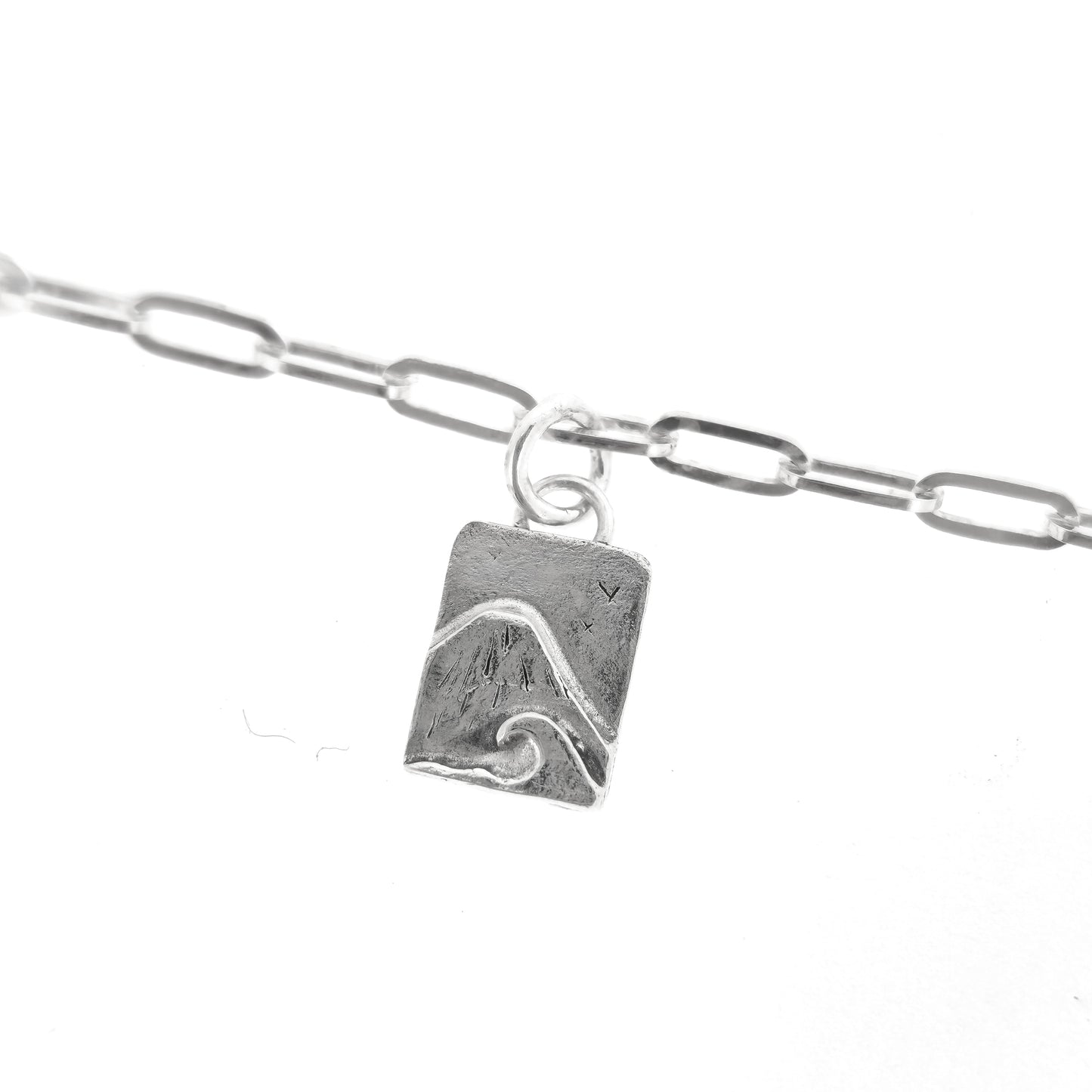 An silver bracelet with oblong links and a rectangular charm featuring a mountain and wave scene.