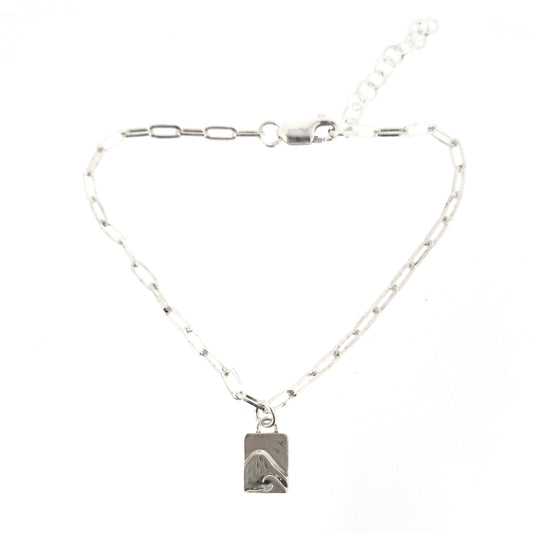 An silver bracelet with oblong links and a rectangular charm featuring a mountain and wave scene.