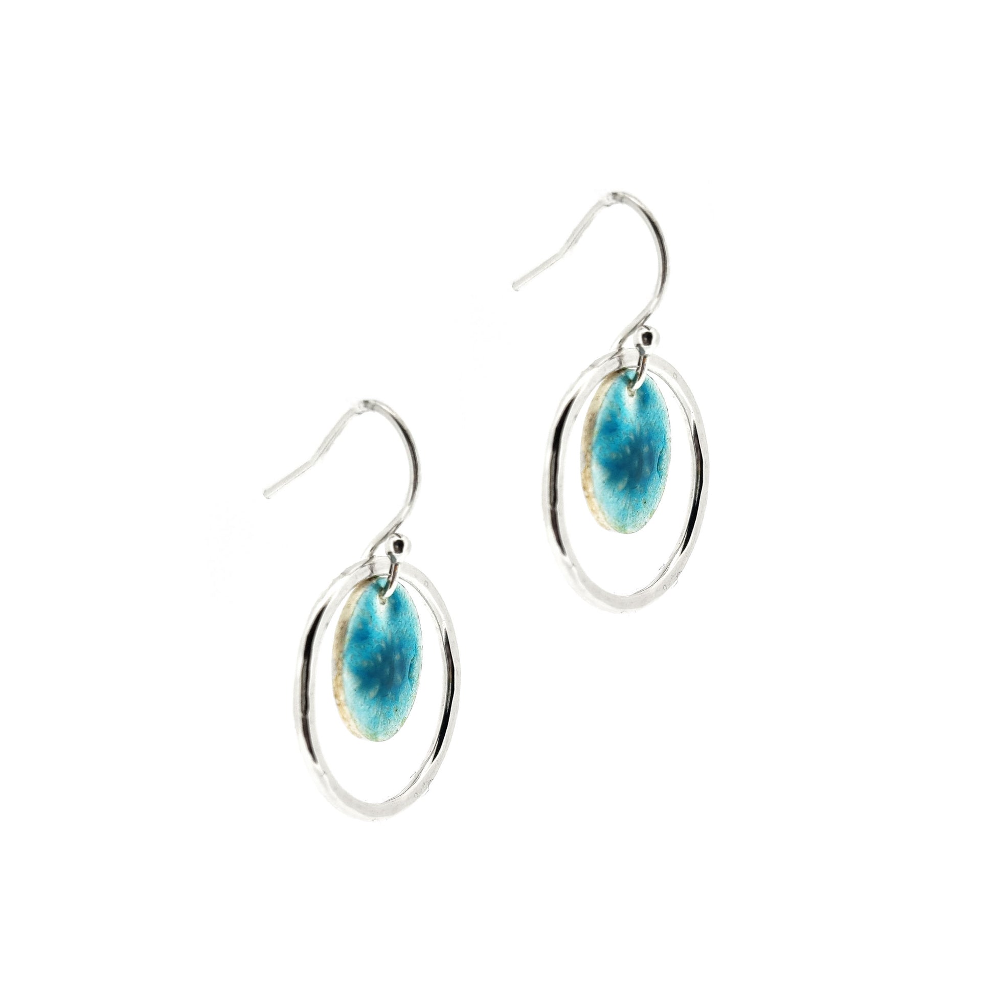 Silver drop earrings with a central silver disc covered with a turquoise enamel pattern and a surrounding hammered silver circle. Side view.