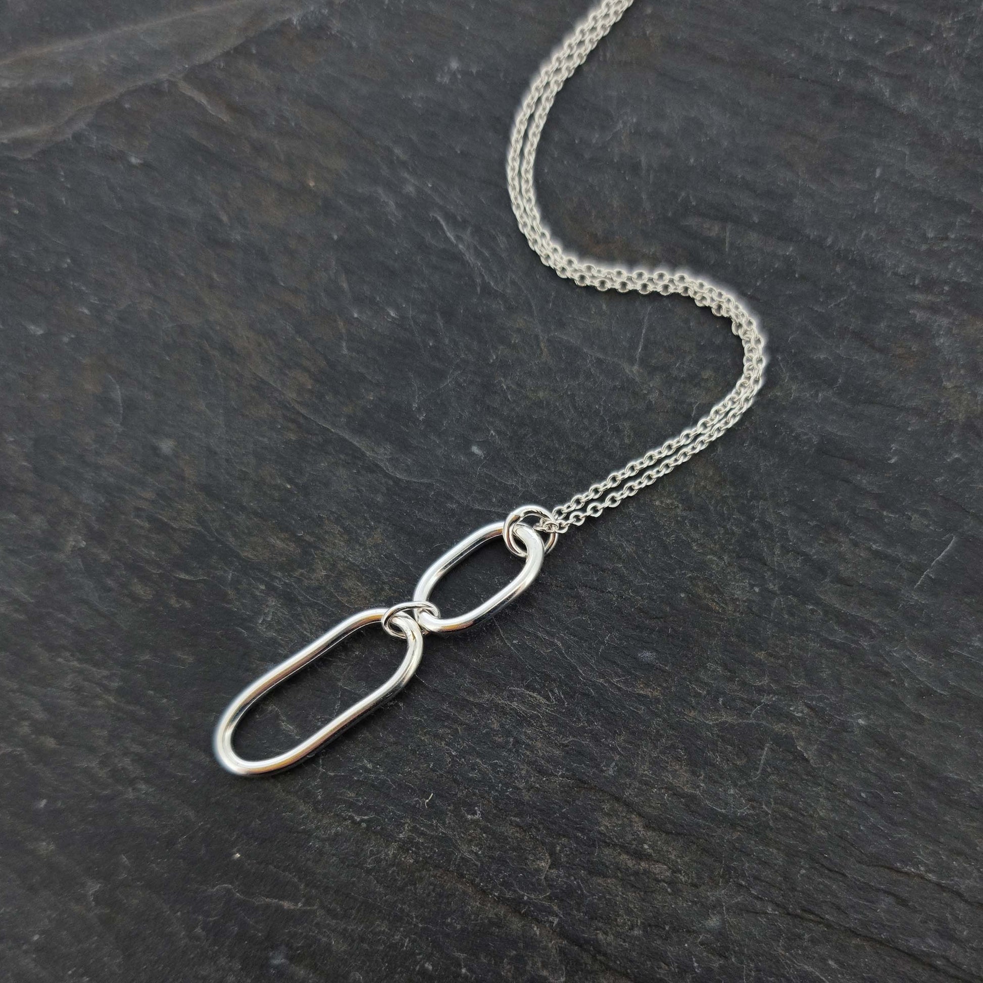 A silver pendant featuring 2 open oblong shapes on a silver chain.