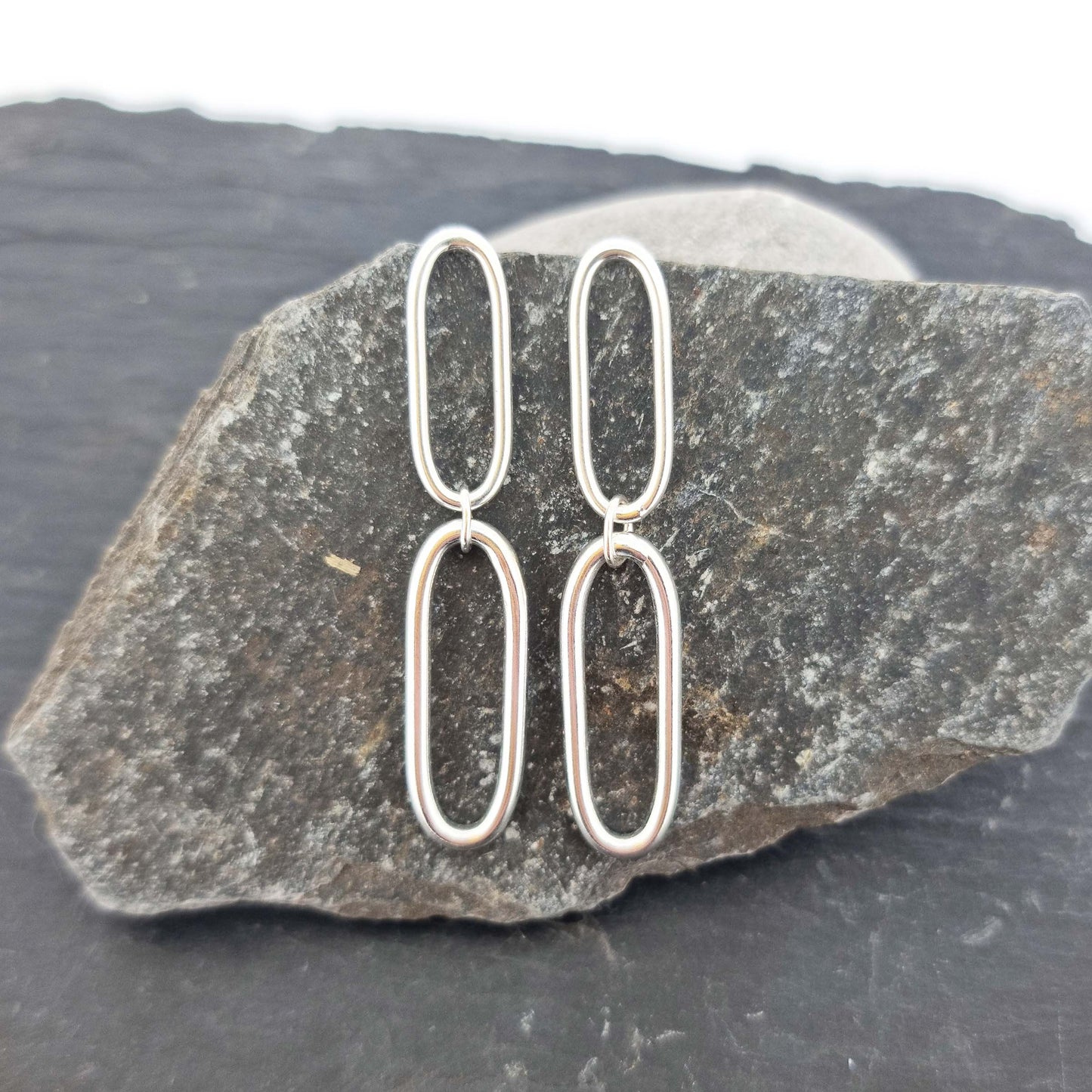 Silver drop earrings featuring 2 open oblong oval shapes attached to each other in a long drop. Shown on a stone.