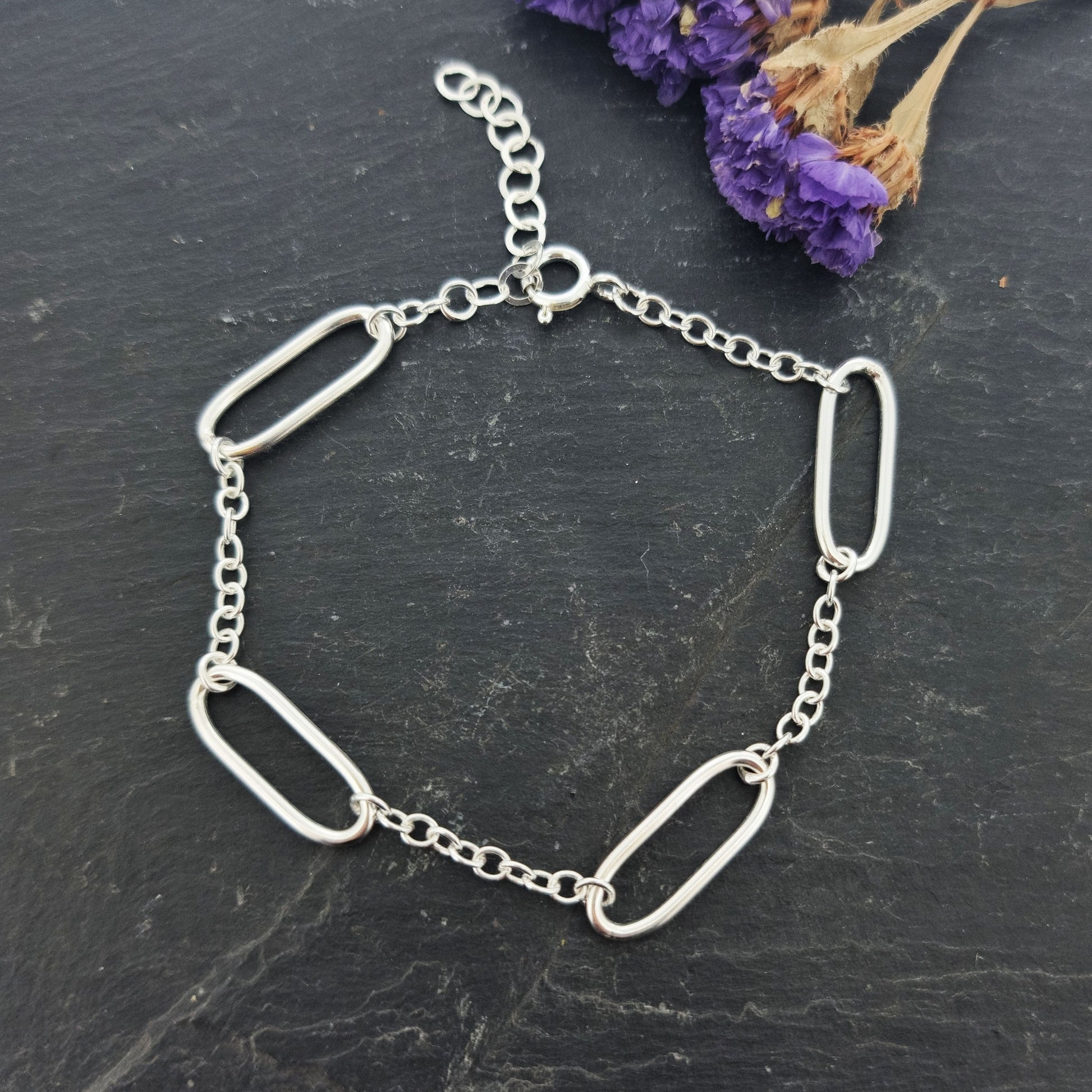 A silver bracelet with 4 oblong oval links set between round linked chain. Pictured on slate with flowers.